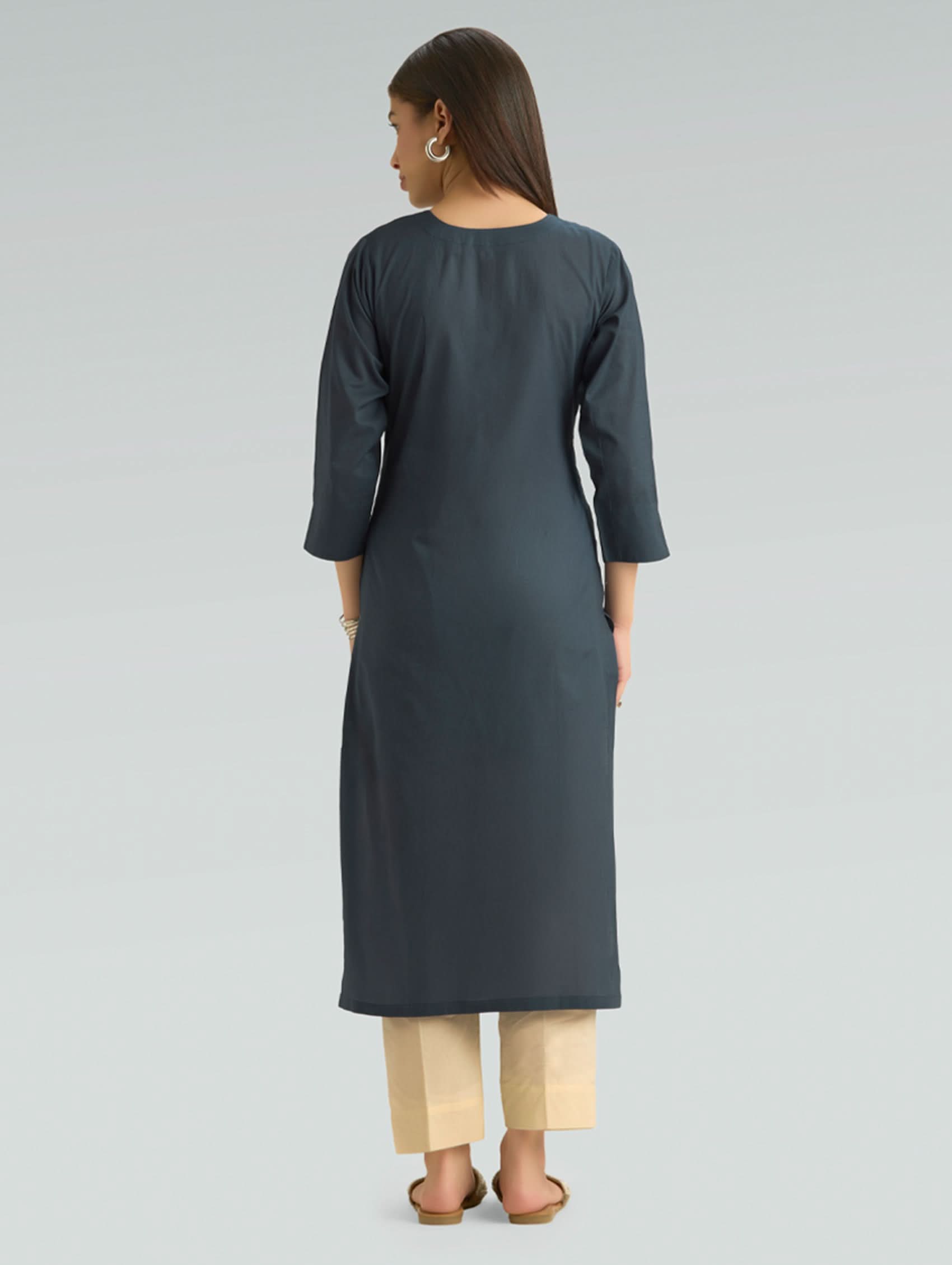 Woman wearing a dark gray kurta with beige pants on a light gray background