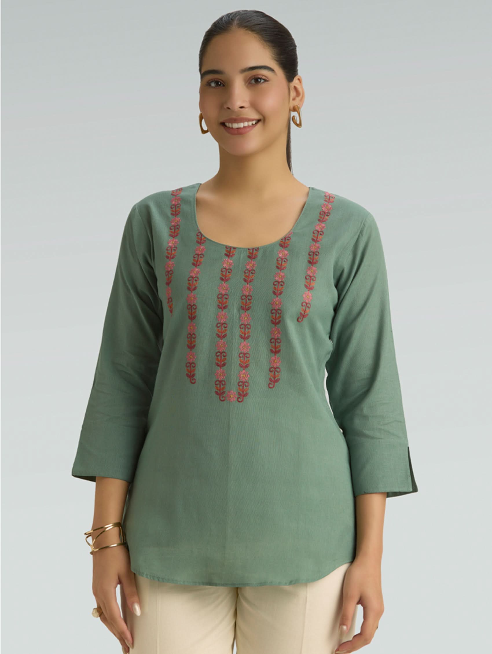 Woman wearing a green embroidered top against a plain background