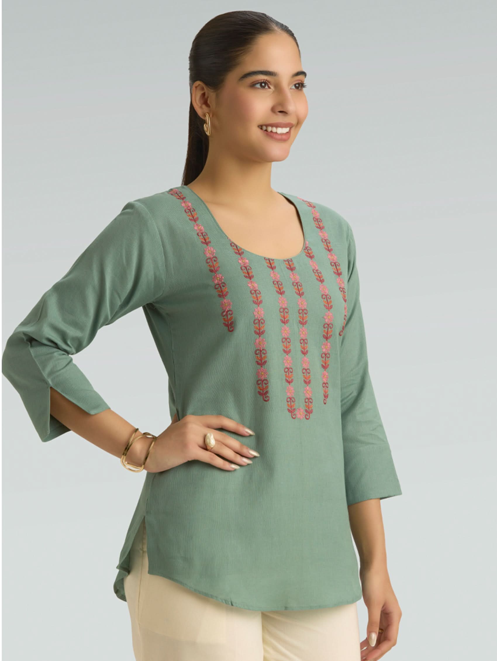 Woman wearing a green top with red embroidery on a light gray background