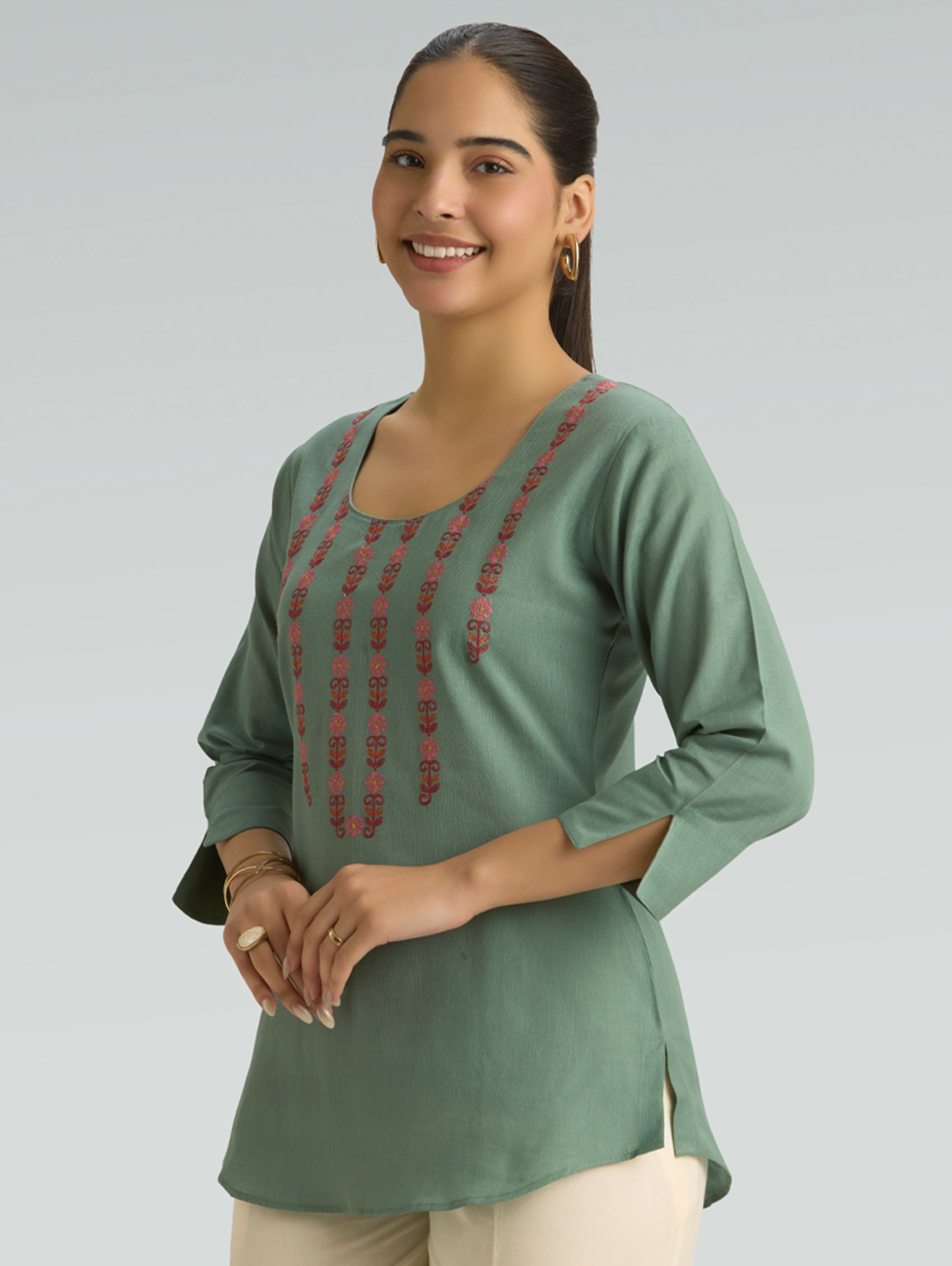 Woman wearing a green top with red embroidery on a gray background