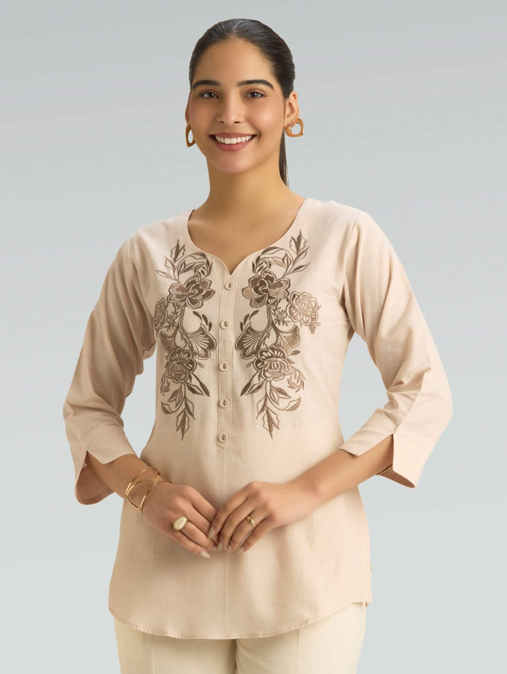 Woman wearing a beige blouse with floral embroidery on a light gray background