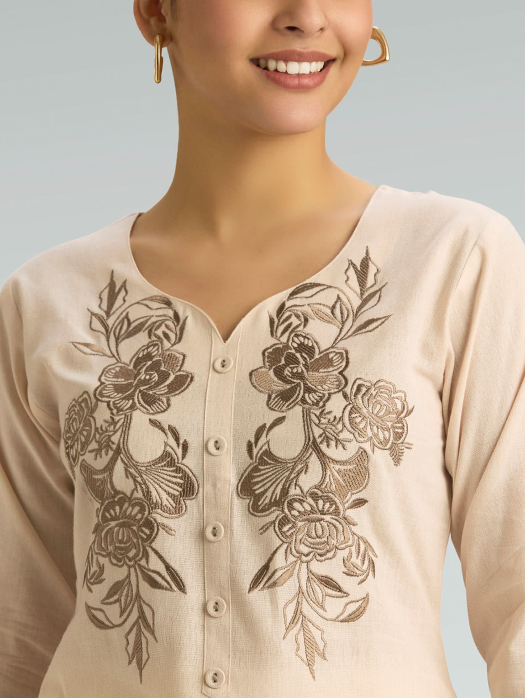 Beige top with floral embroidery on a plain background
