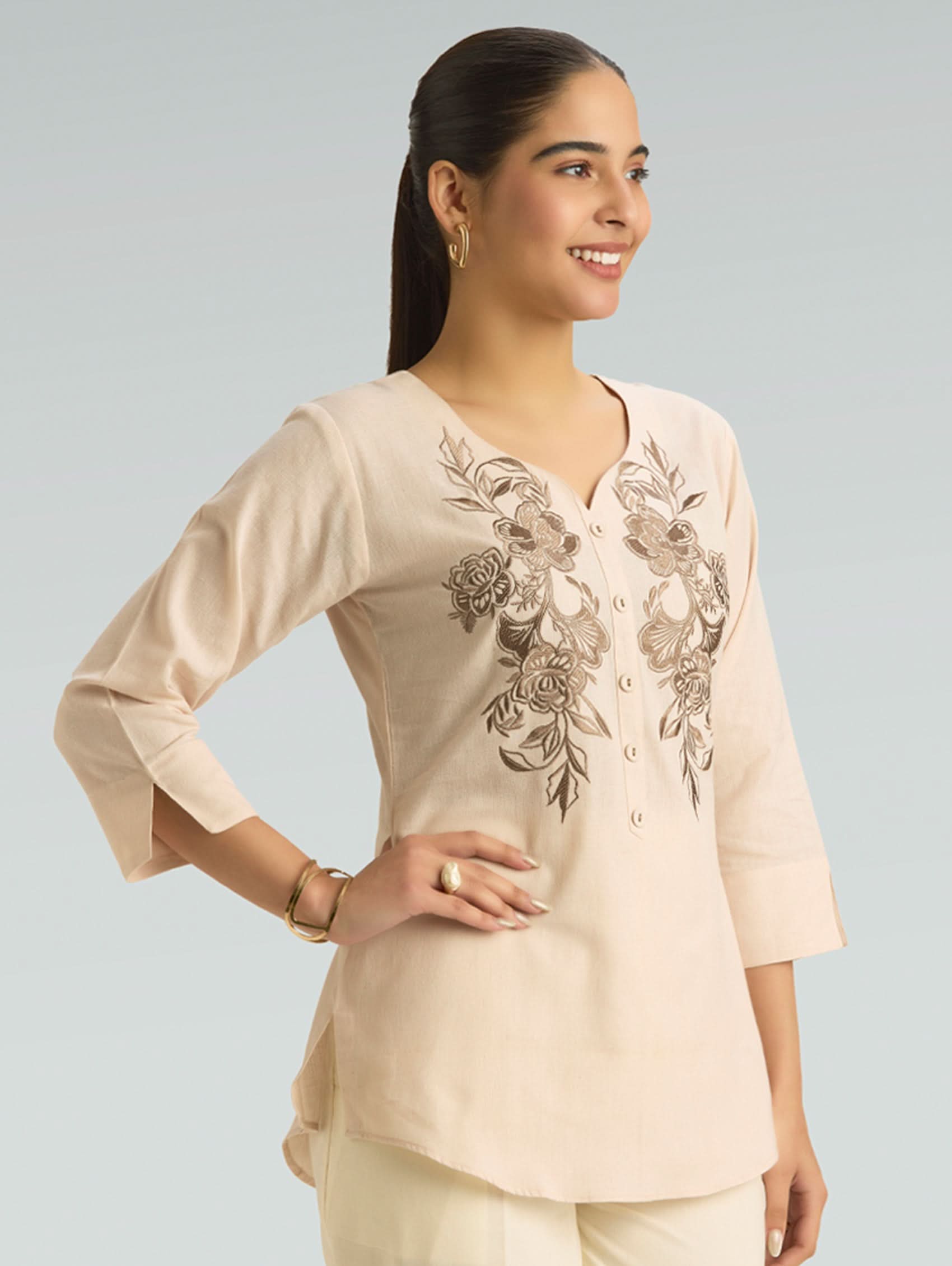 Woman wearing a beige embroidered top with a plain background