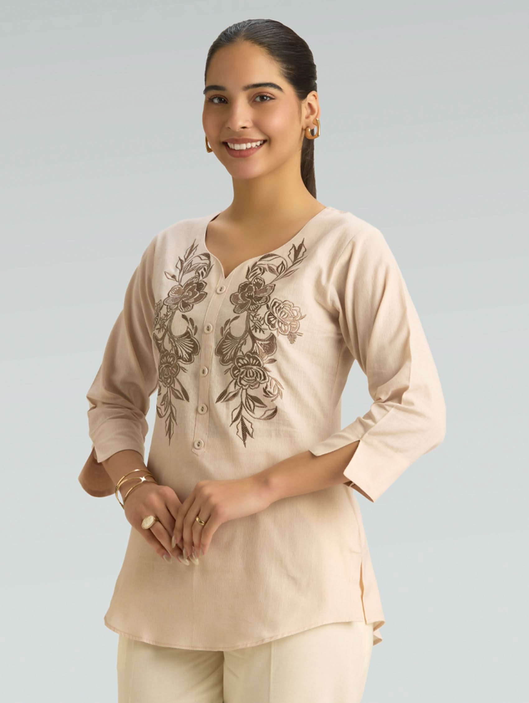 Woman wearing a beige top with floral embroidery on a plain background