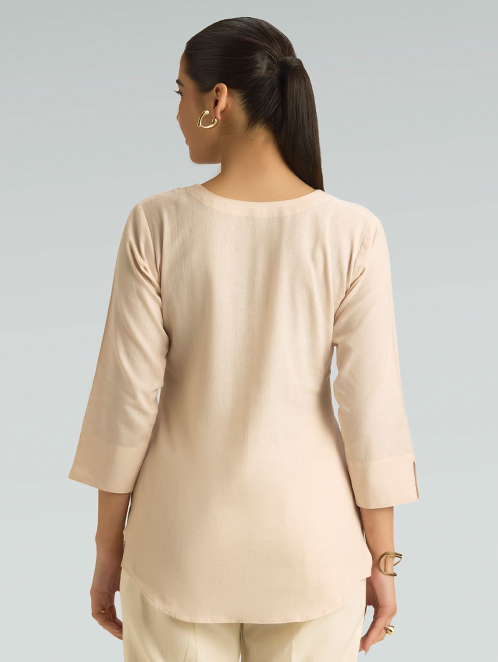 Woman wearing a beige top and pants against a gray background