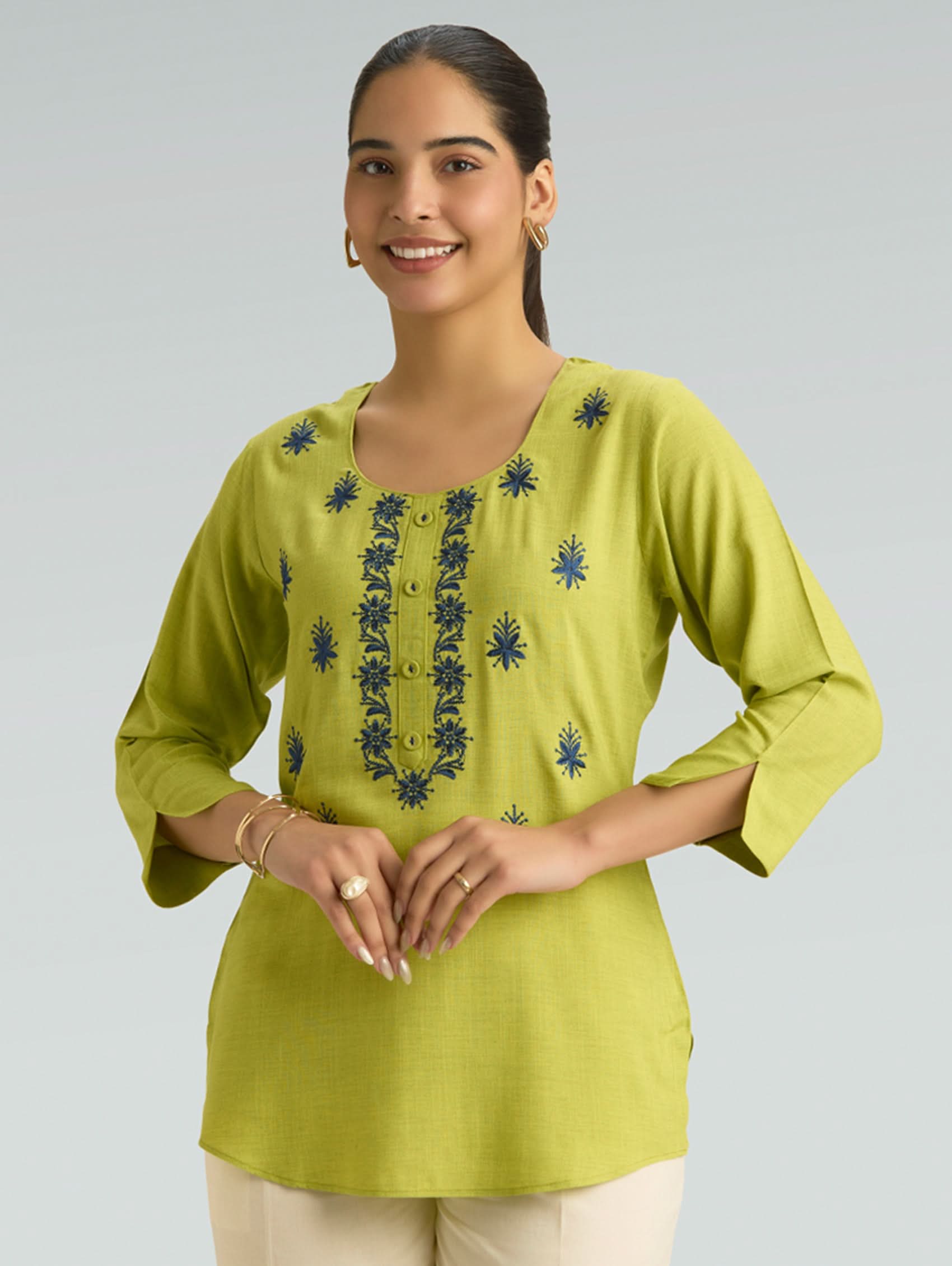 Woman wearing a green embroidered top against a gray background