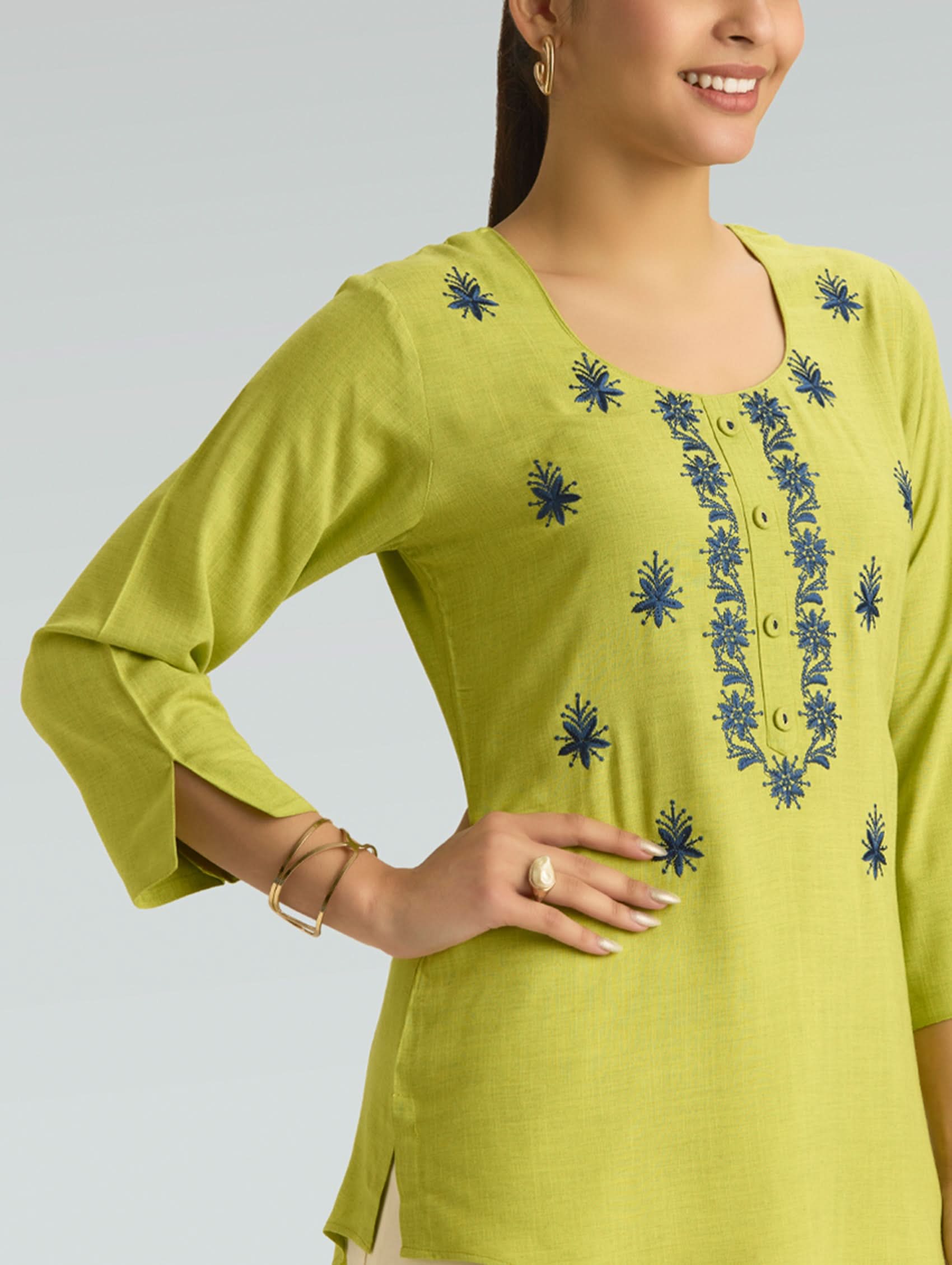 Woman wearing a green embroidered top against a gray background