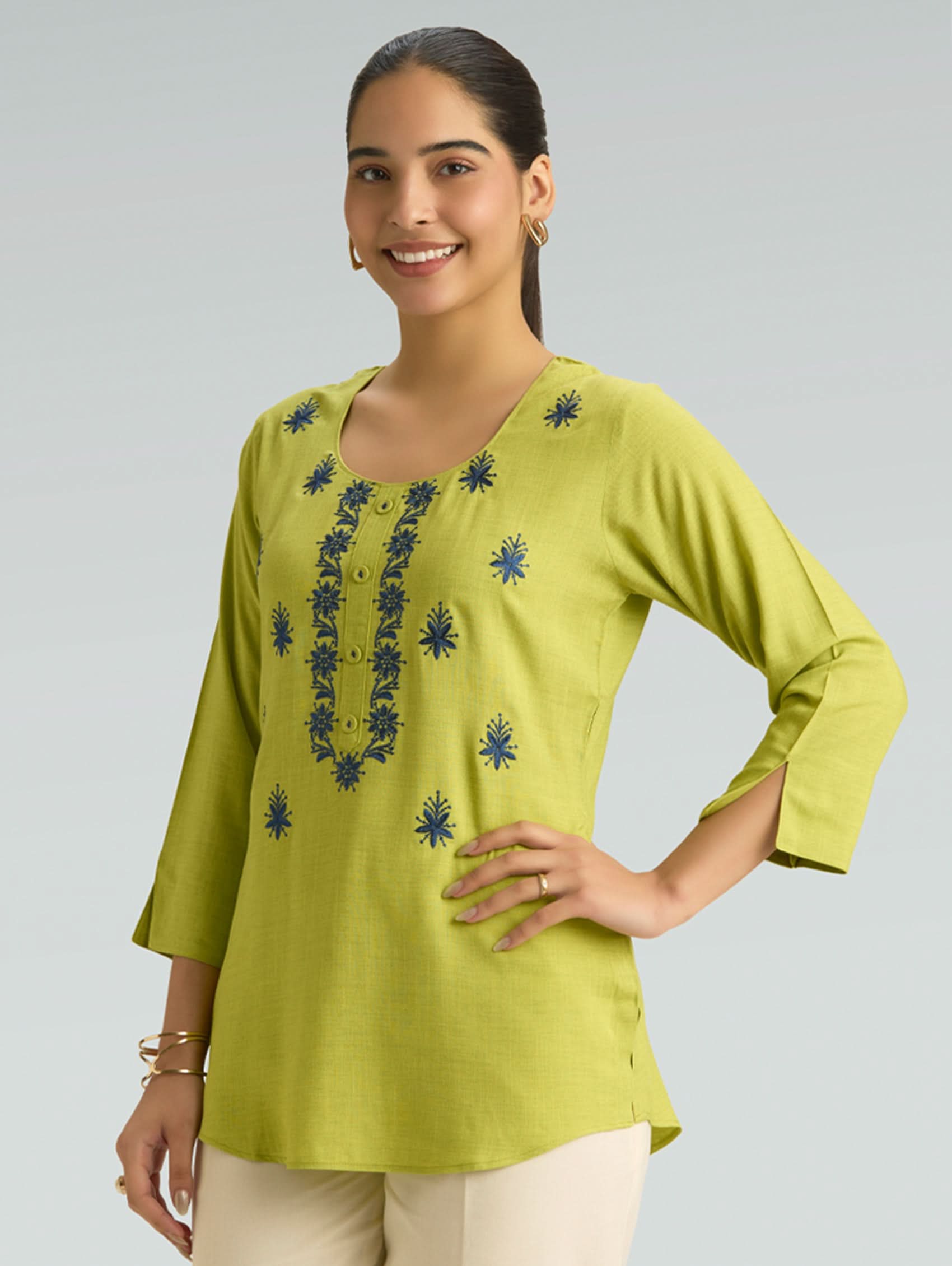Woman wearing a green embroidered top on a gray background