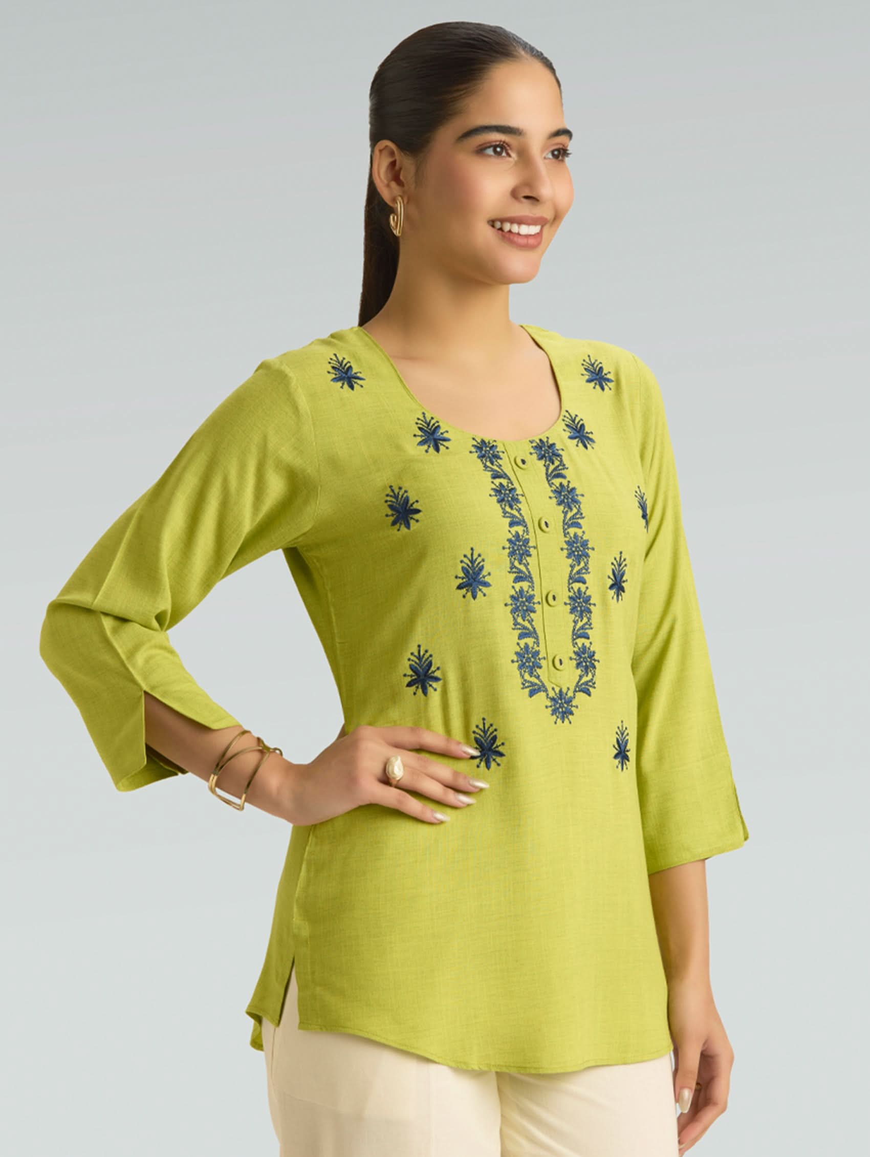 Woman wearing a green embroidered top against a gray background