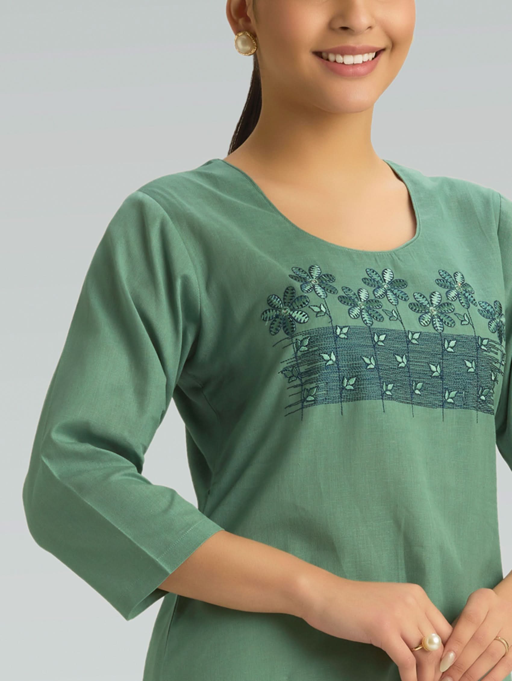 Woman wearing a green embroidered top against a gray background