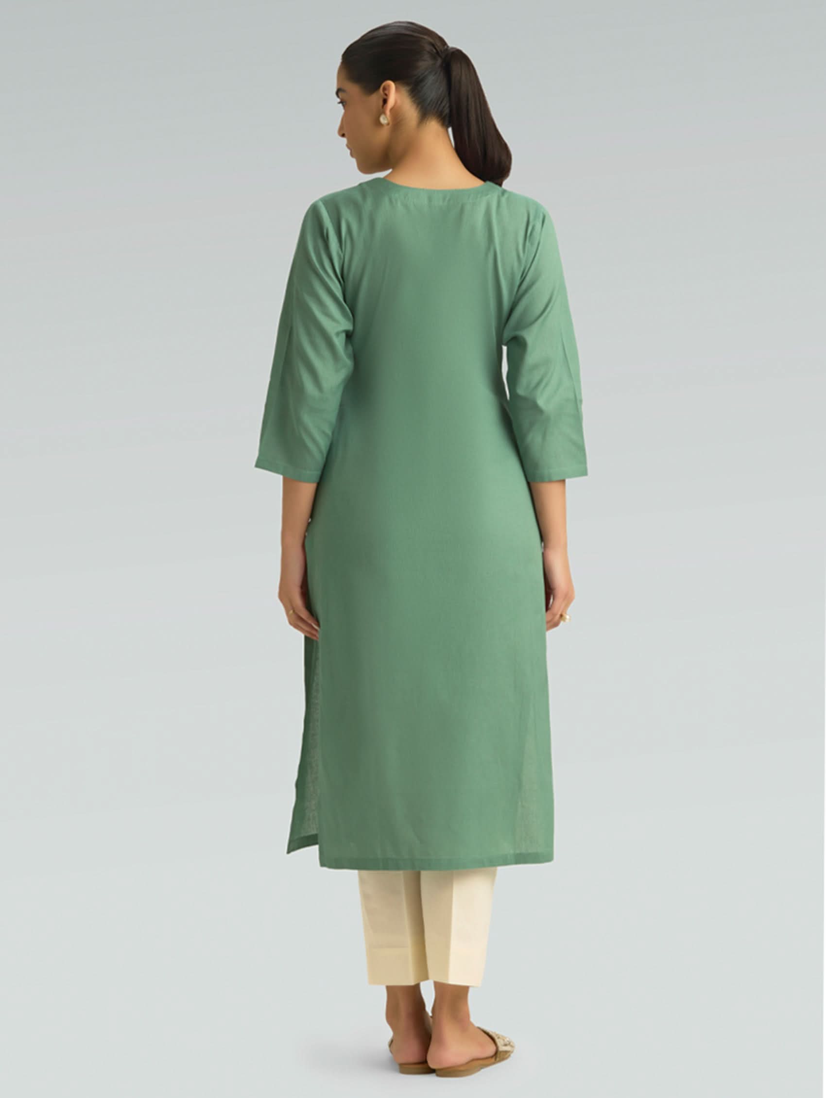 Woman wearing a green kurta with beige pants on a light gray background