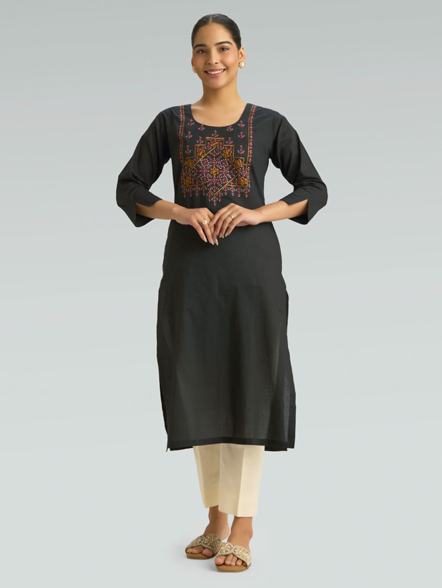 Woman wearing a black kurta with intricate embroidery on a gray background