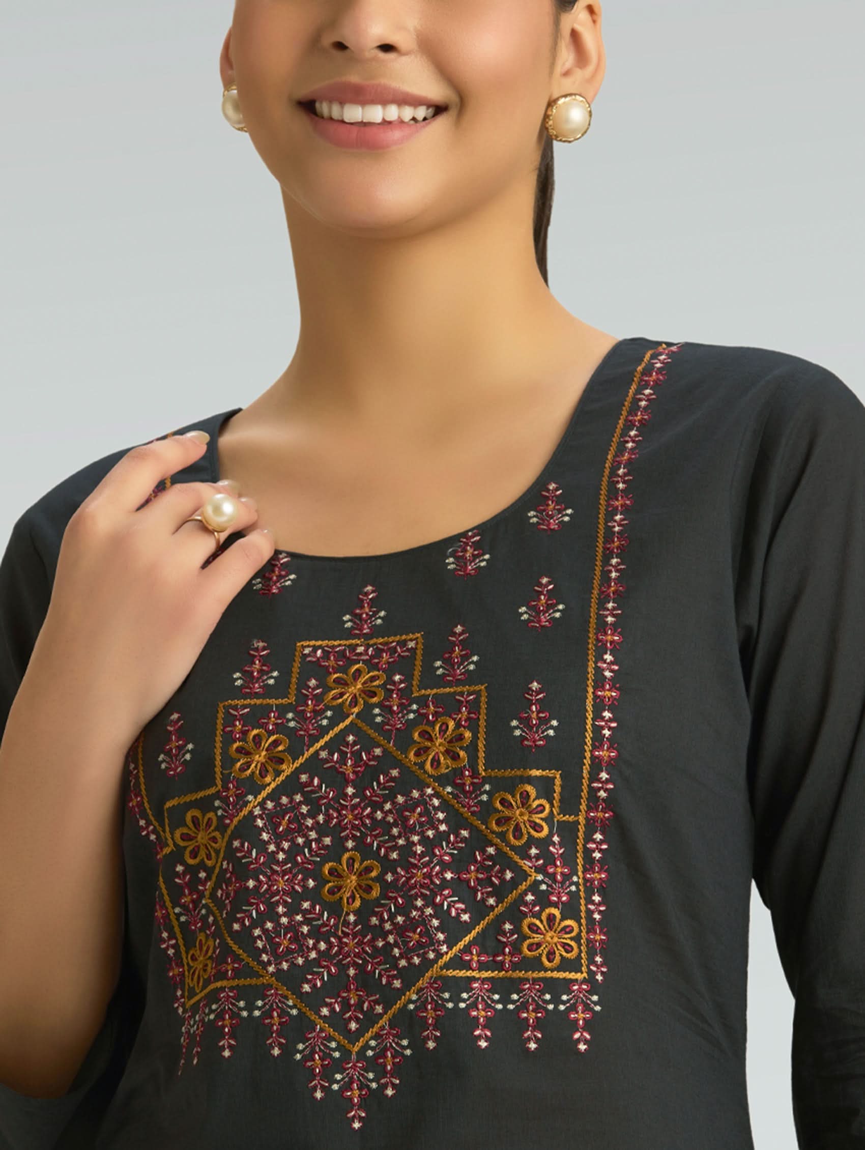 Woman wearing a black top with intricate floral embroidery on a plain background