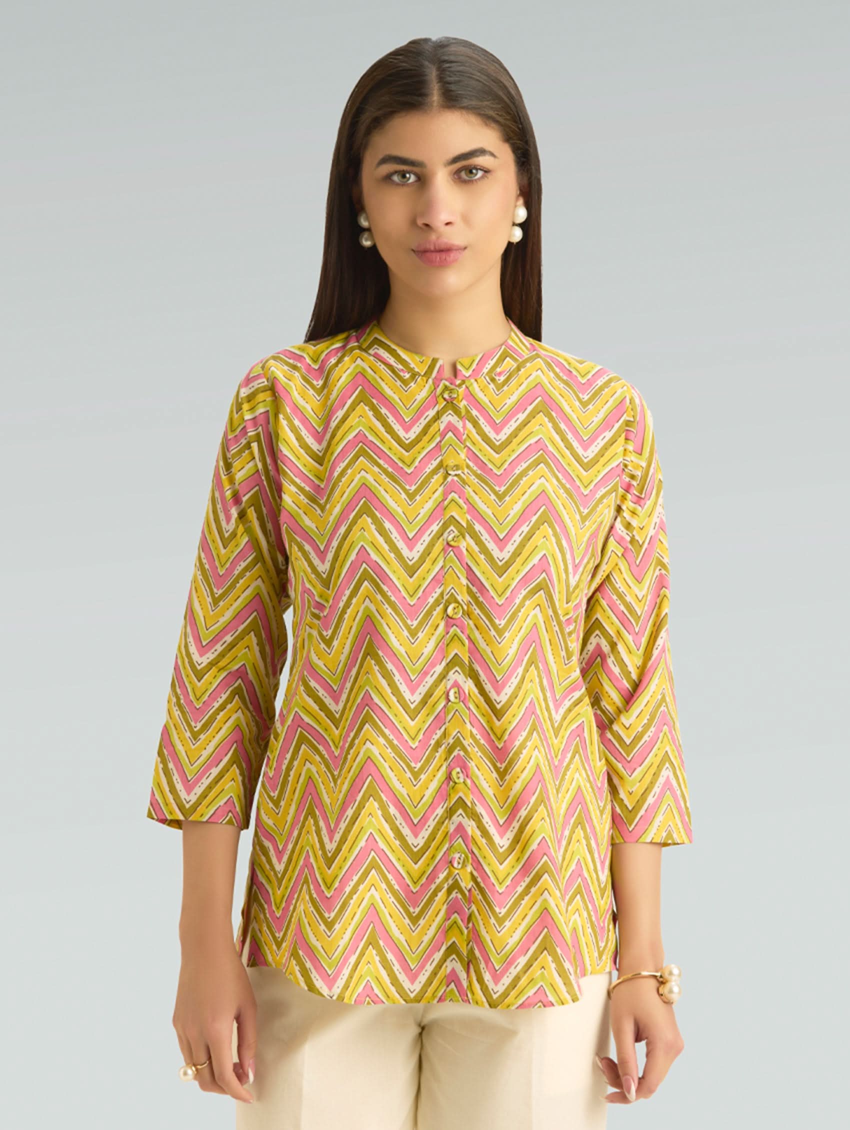Woman wearing a yellow and pink zigzag patterned shirt on a gray background