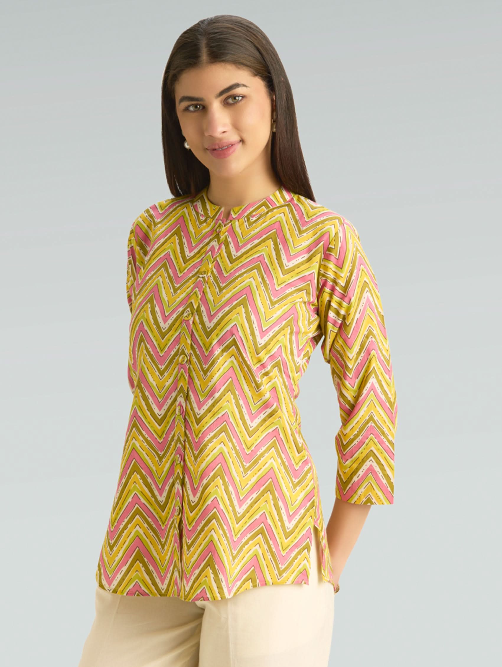 Woman wearing a yellow and pink chevron patterned top on a gray background
