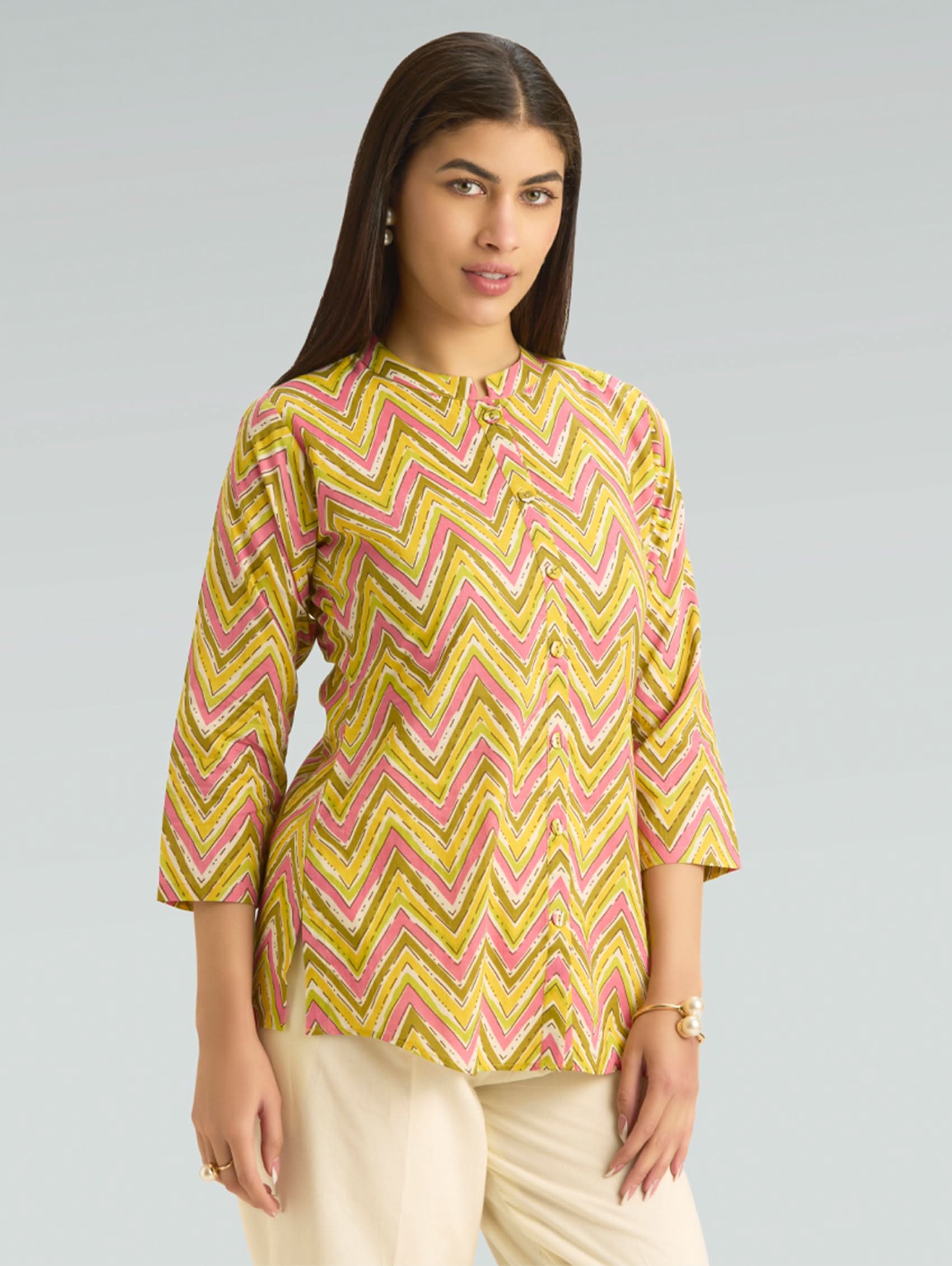 Woman wearing a yellow and pink zigzag patterned top on a gray background