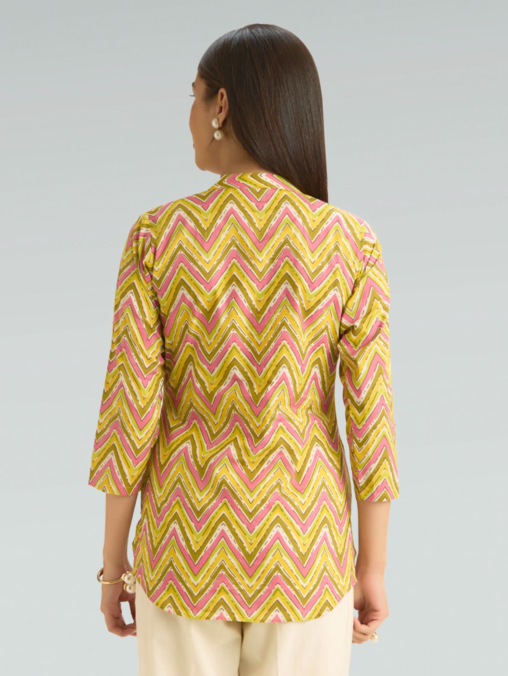 Woman wearing a yellow and pink zigzag patterned top on a gray background