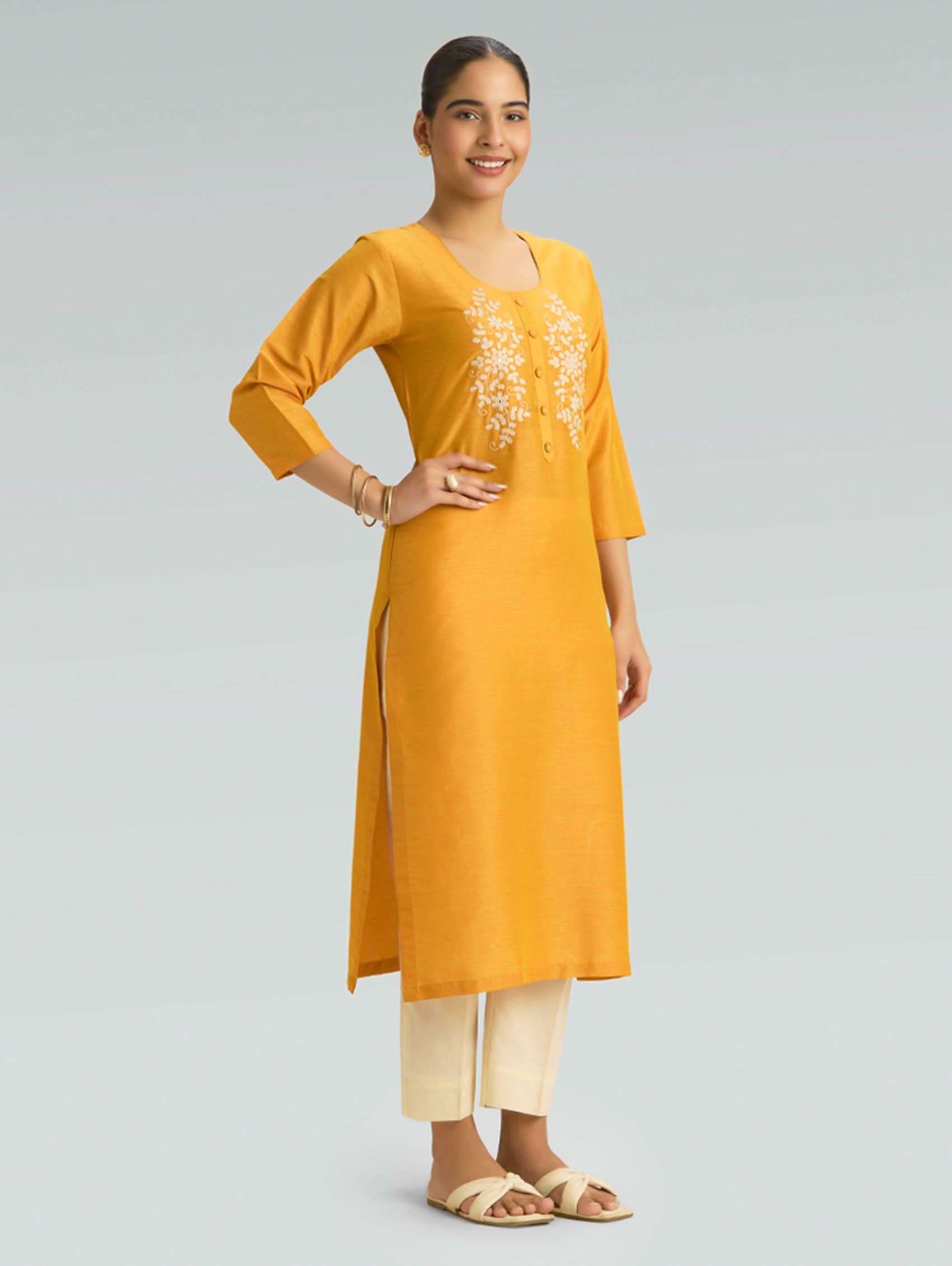 A woman wearing a Moon yellow kurta with side slit and white pants on a gray background