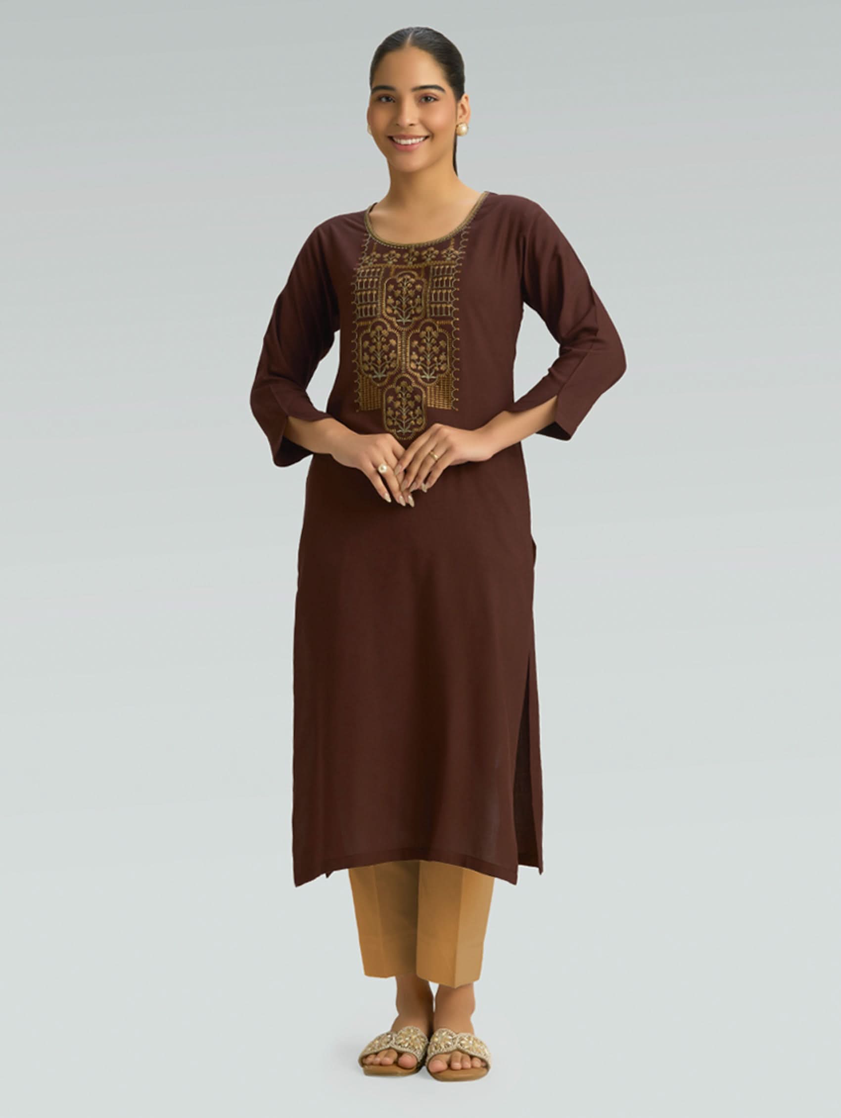 Woman wearing a brown straight-fit kurta with computer-thread embroidery, round neckline, and 3/4 sleeves on a grey background