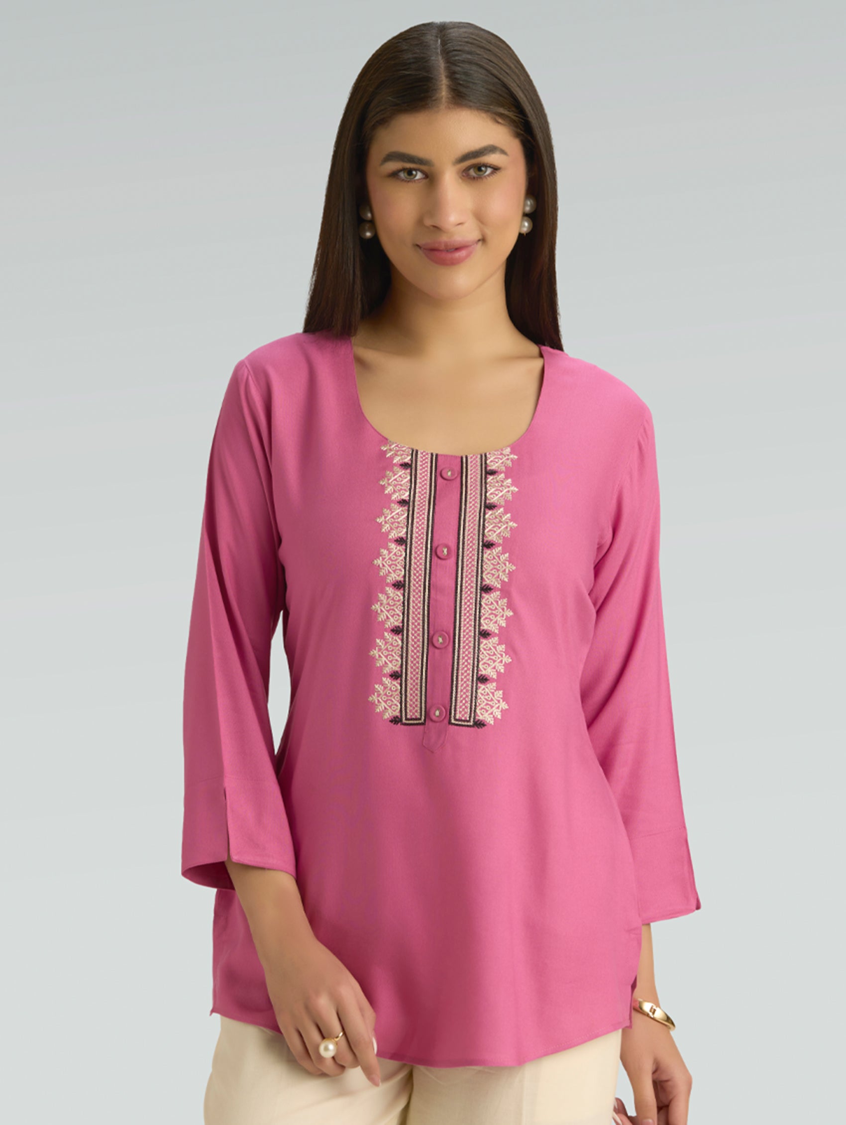Woman wearing a pink embroidered top on a gray background