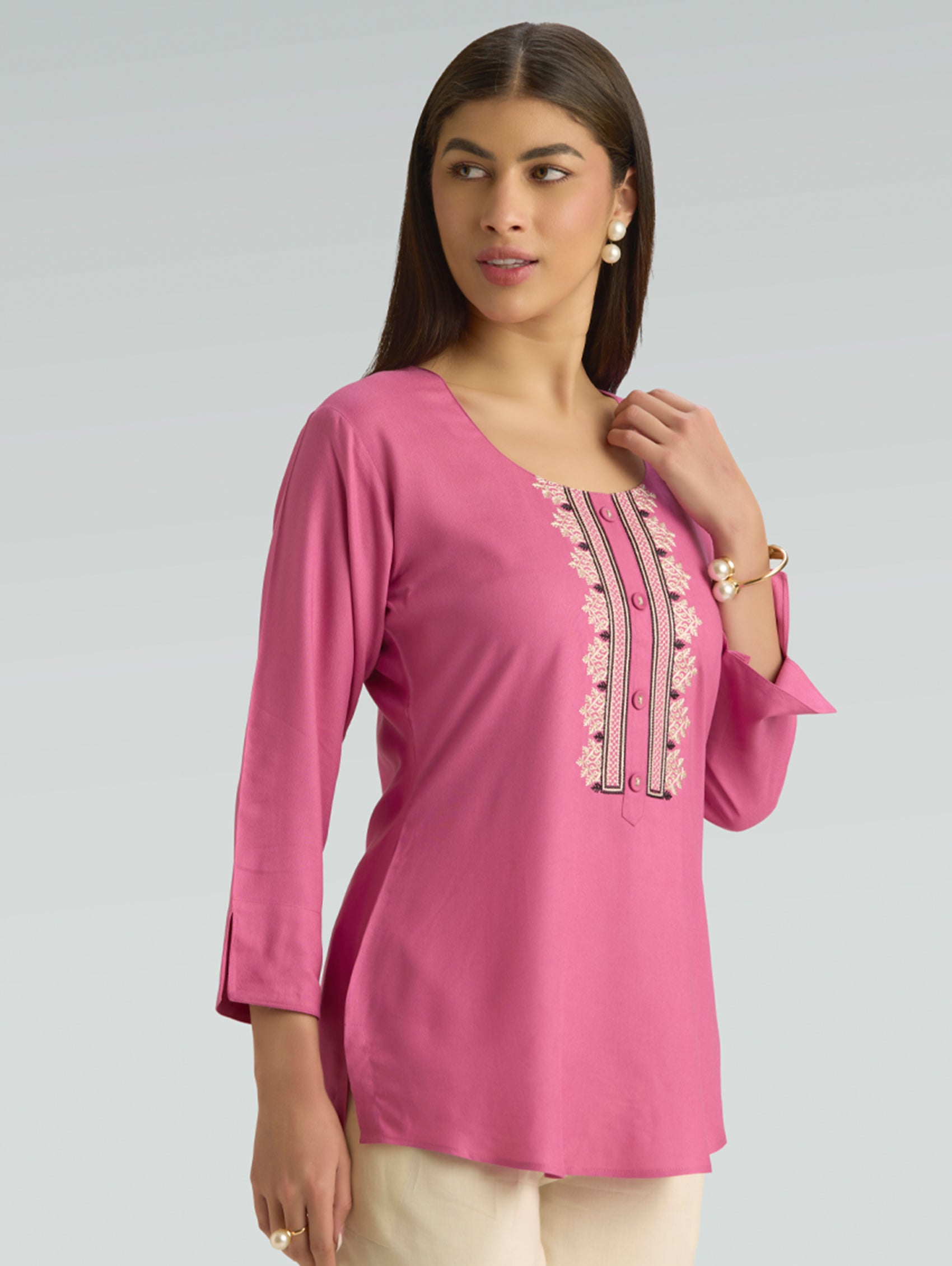 Woman wearing a pink embroidered top on a gray background