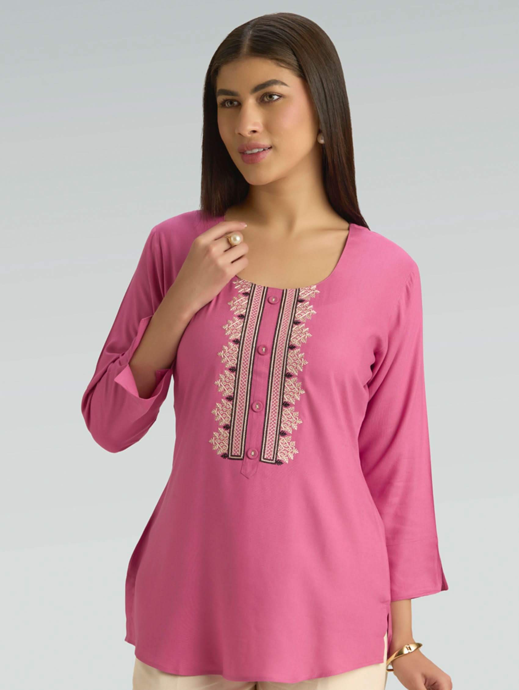 Woman wearing a pink embroidered kurti against a gray background