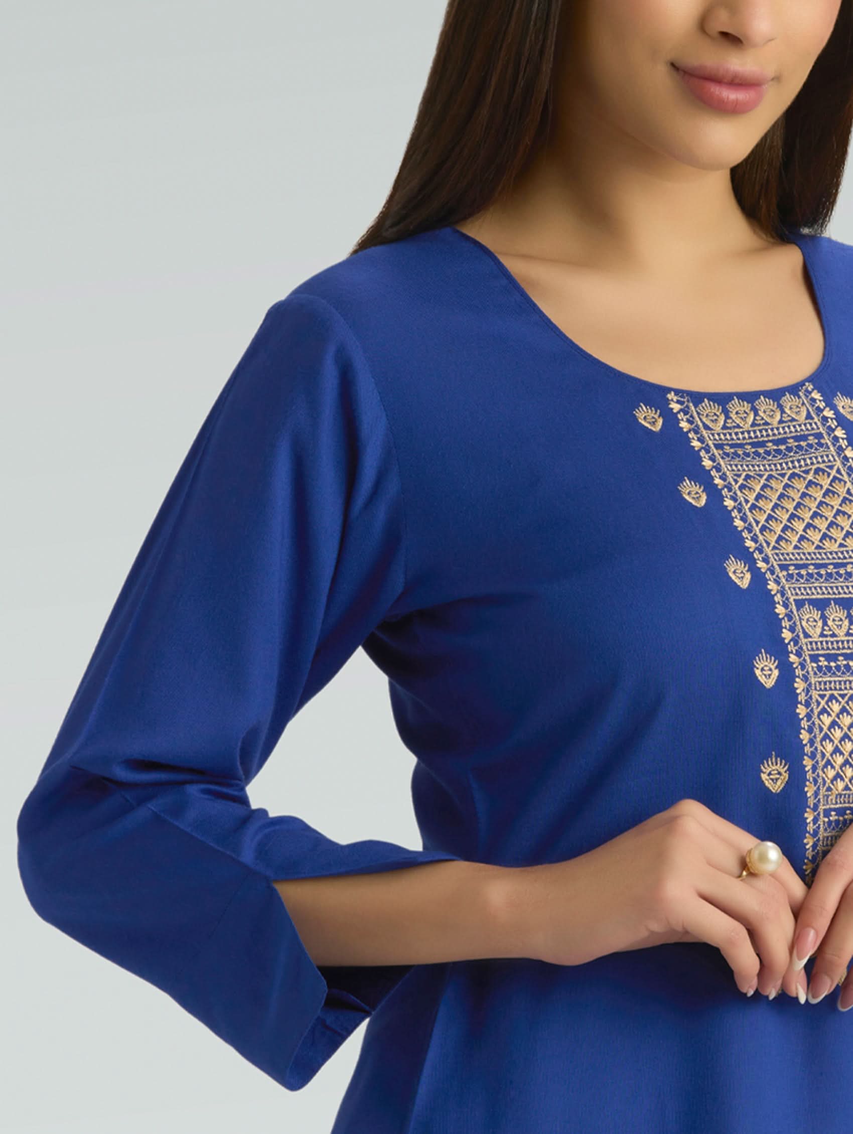 Blue top with intricate gold embroidery on a plain background
