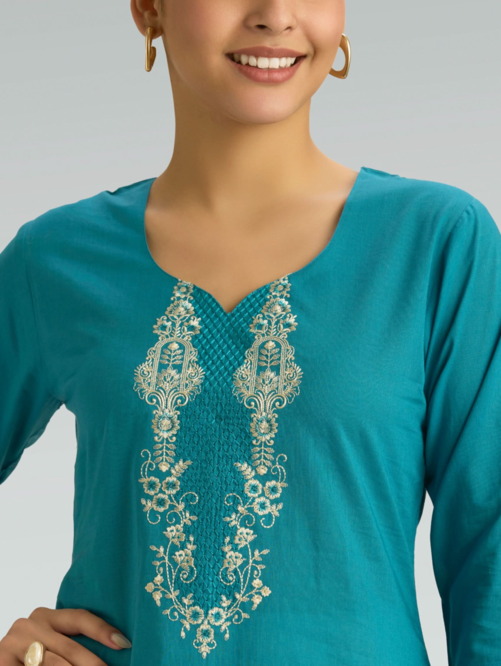 Teal top with intricate white embroidery on a plain background
