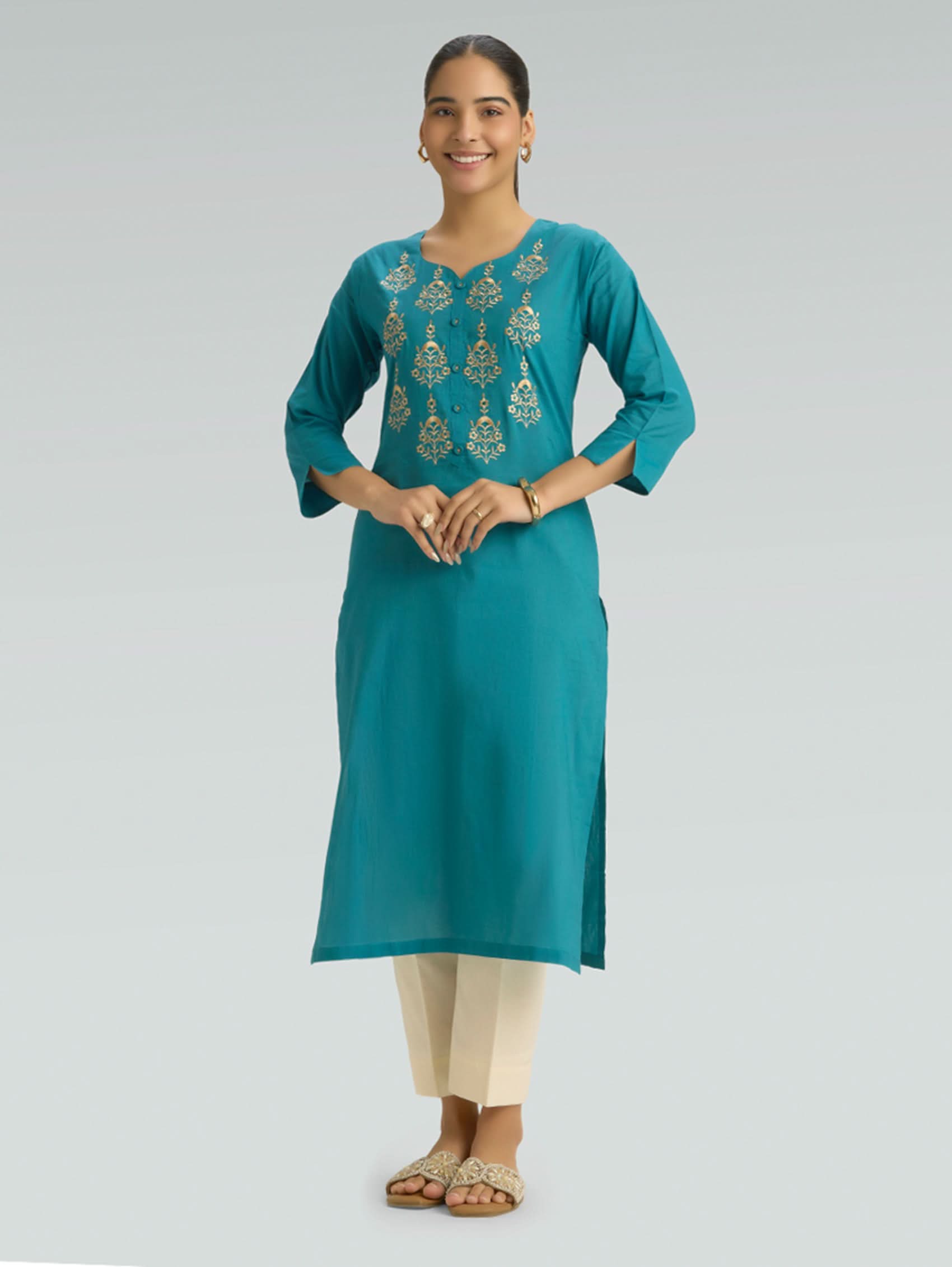 A woman wearing an Iris Blue Colour kurta with computer thread embroidered and a round neckline with 3/4 Sleeves with a side Slit and beige pants on a grey background