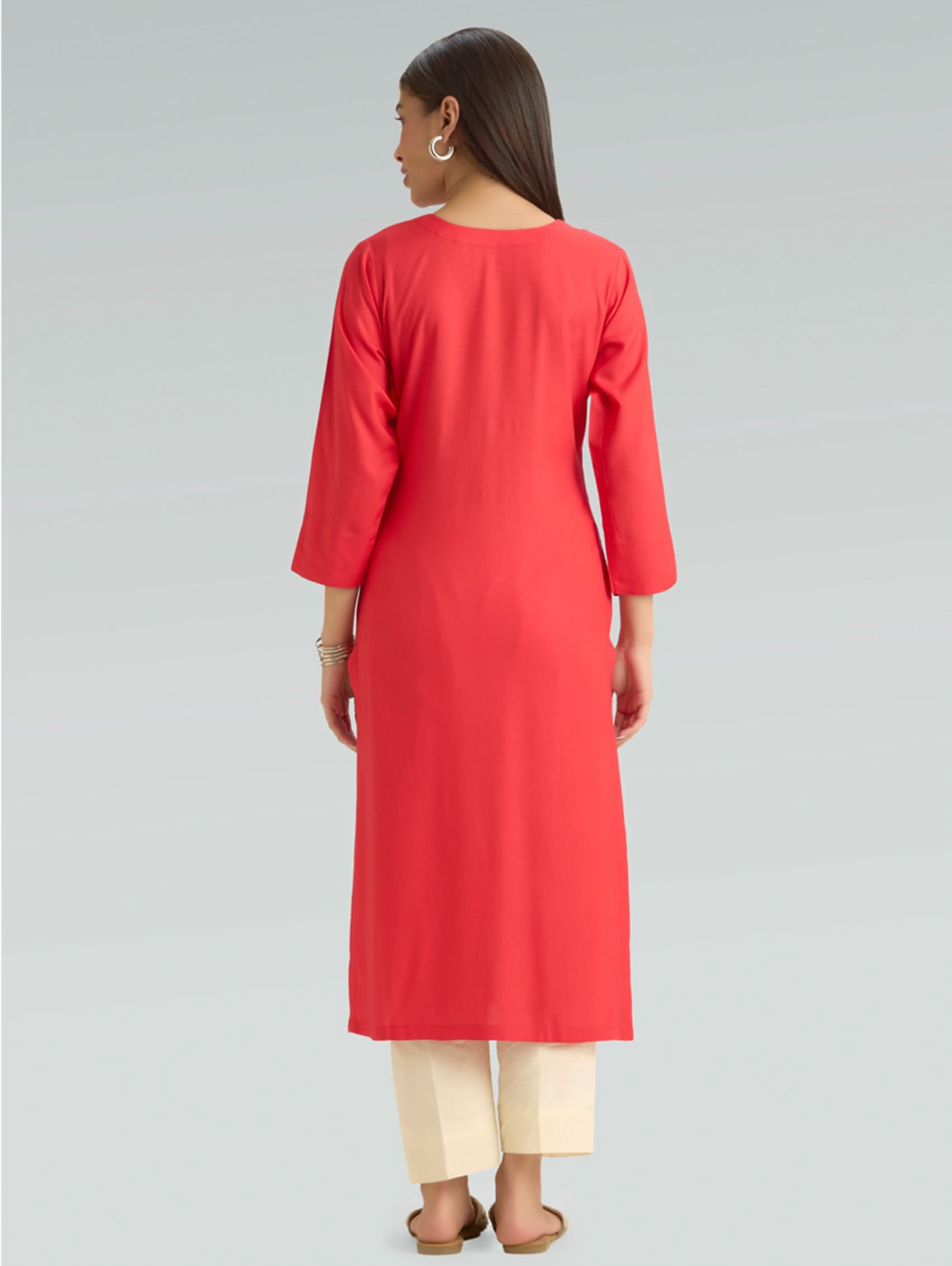Woman wearing a red kurta with beige pants on a gray background