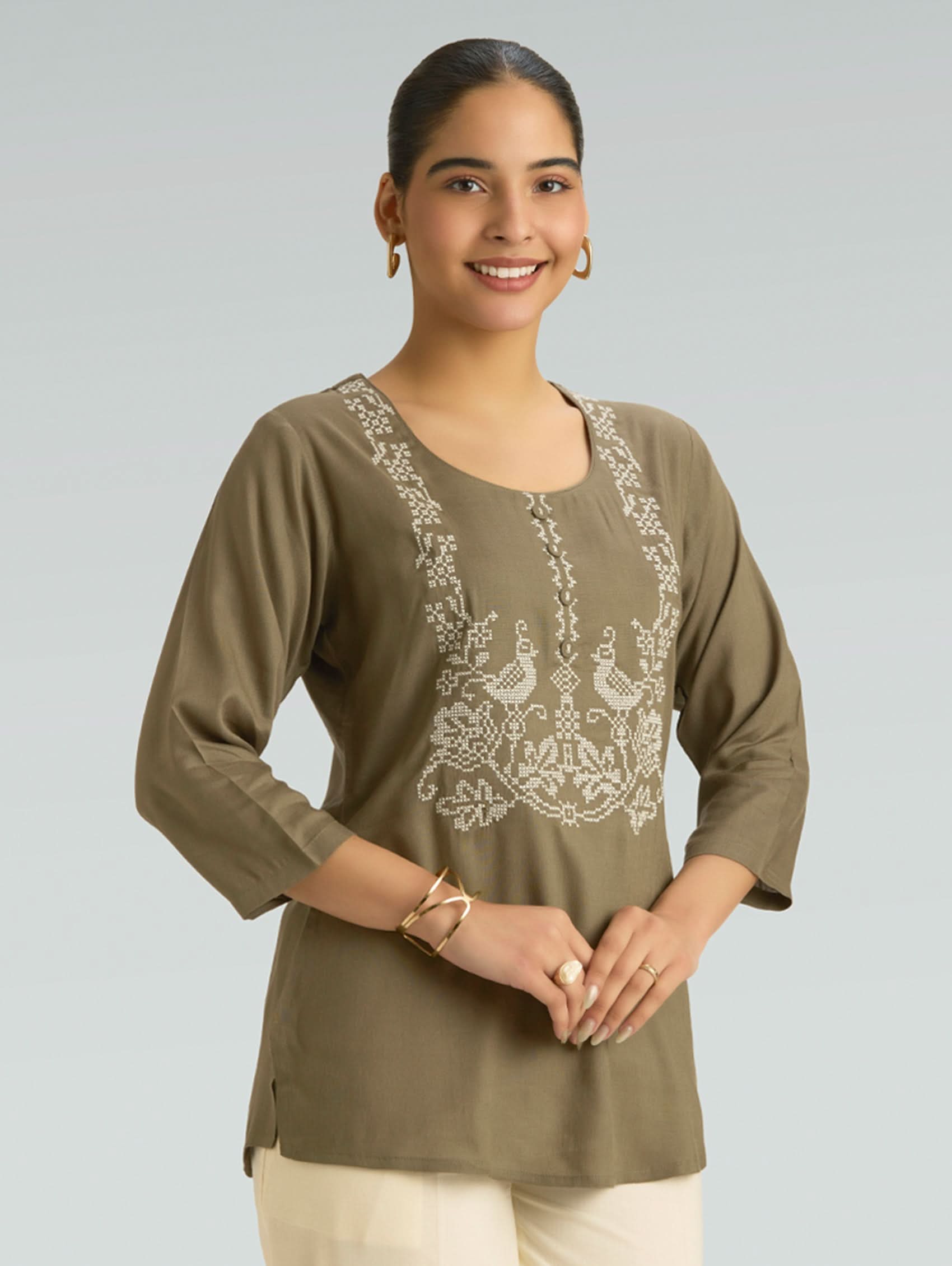Woman wearing an olive green embroidered top against a plain background