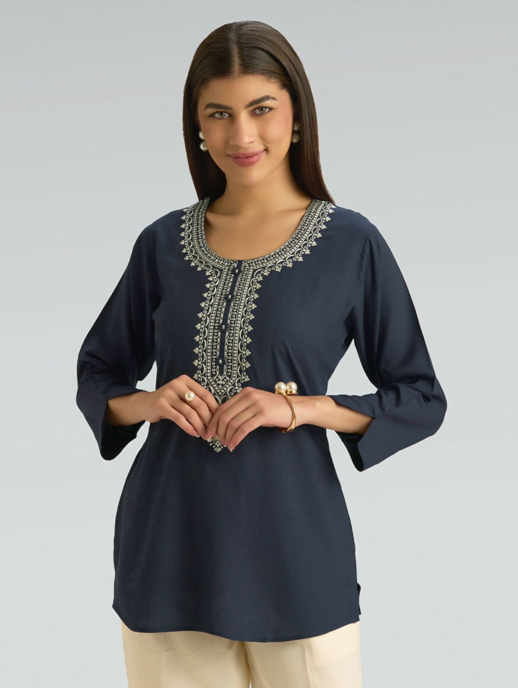 Woman wearing a navy blue embroidered top on a gray background