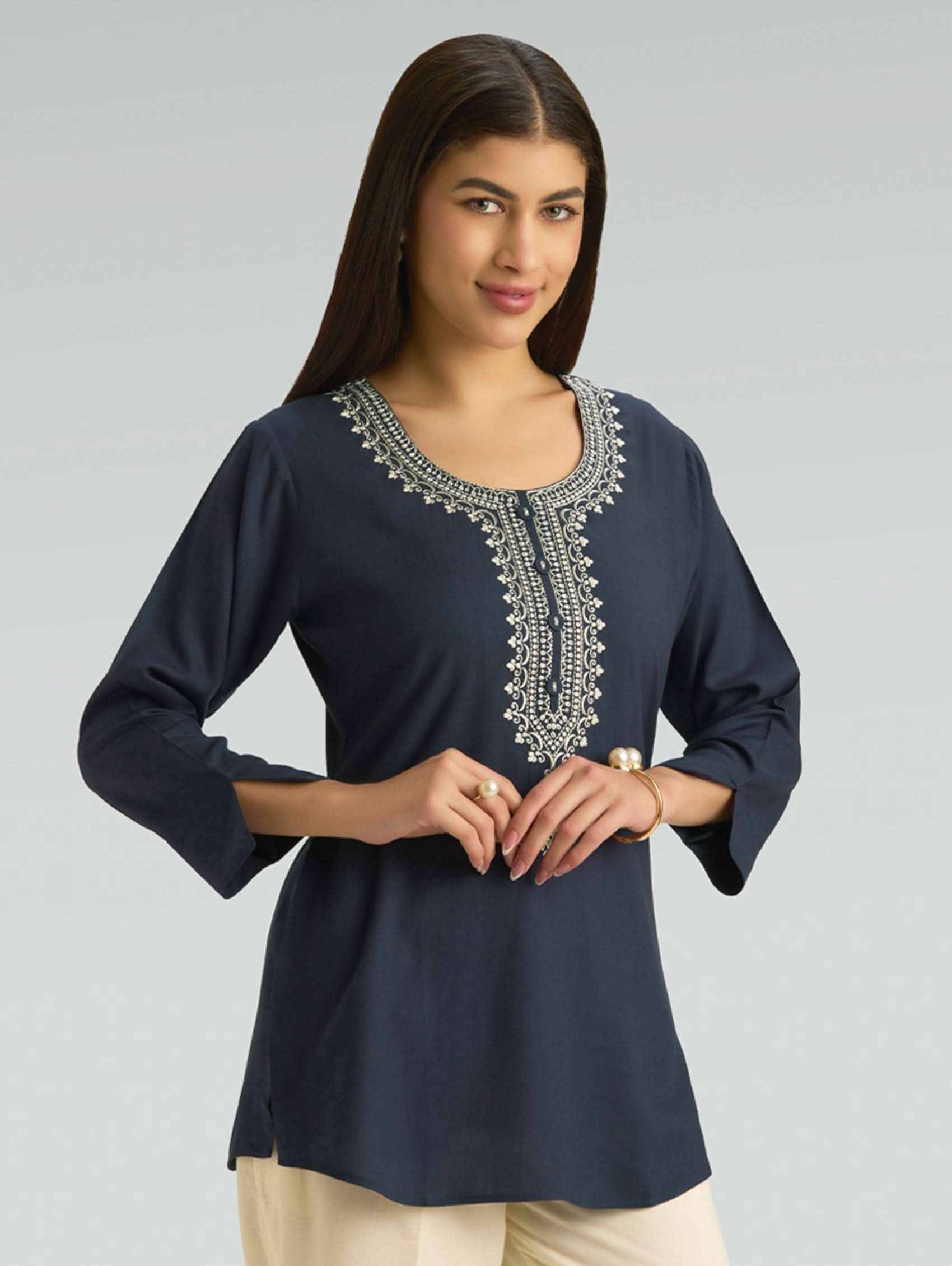 Woman wearing a navy blue top with intricate white embroidery on a gray background