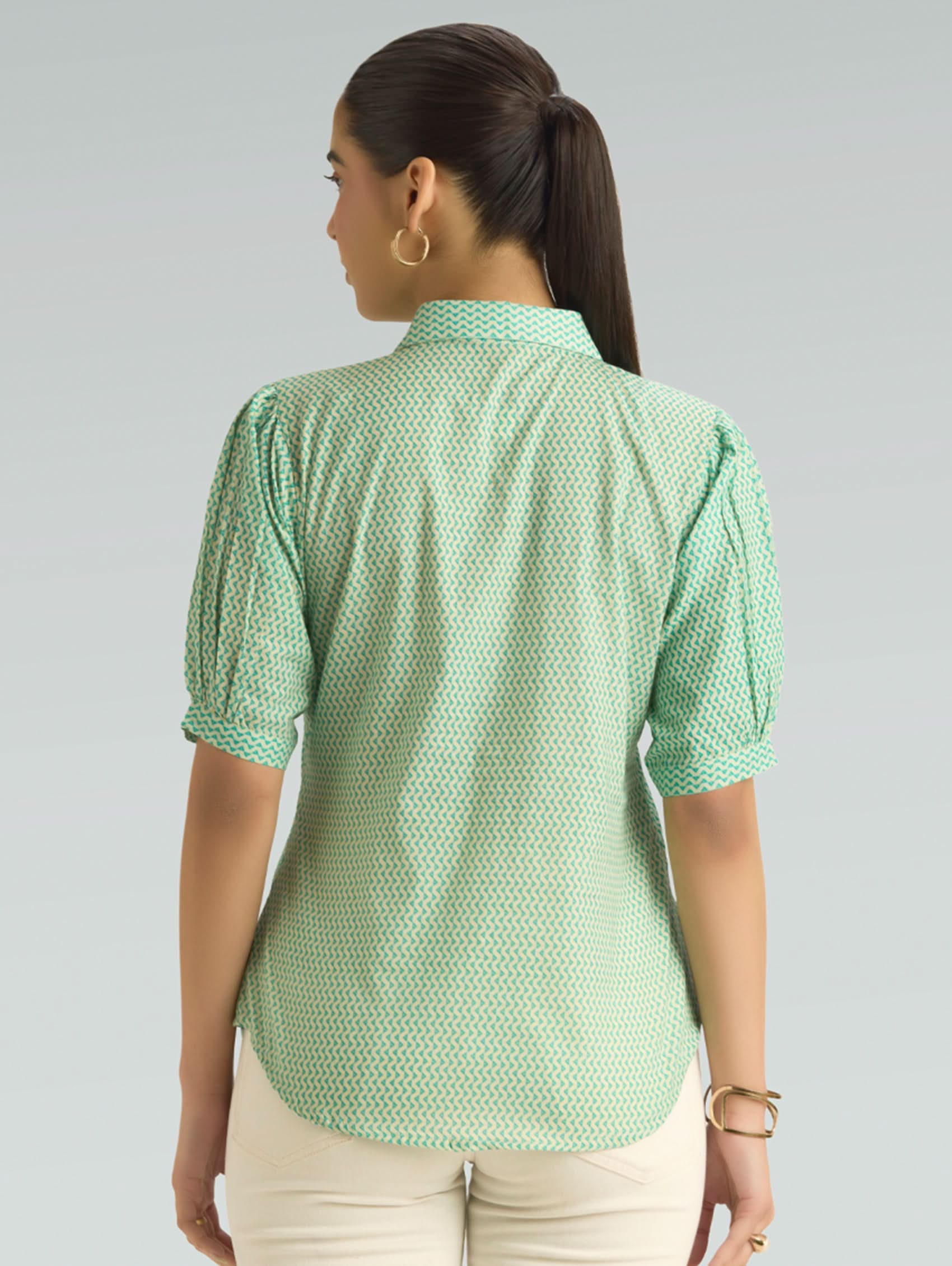 Woman wearing a green patterned shirt from behind on a gray background