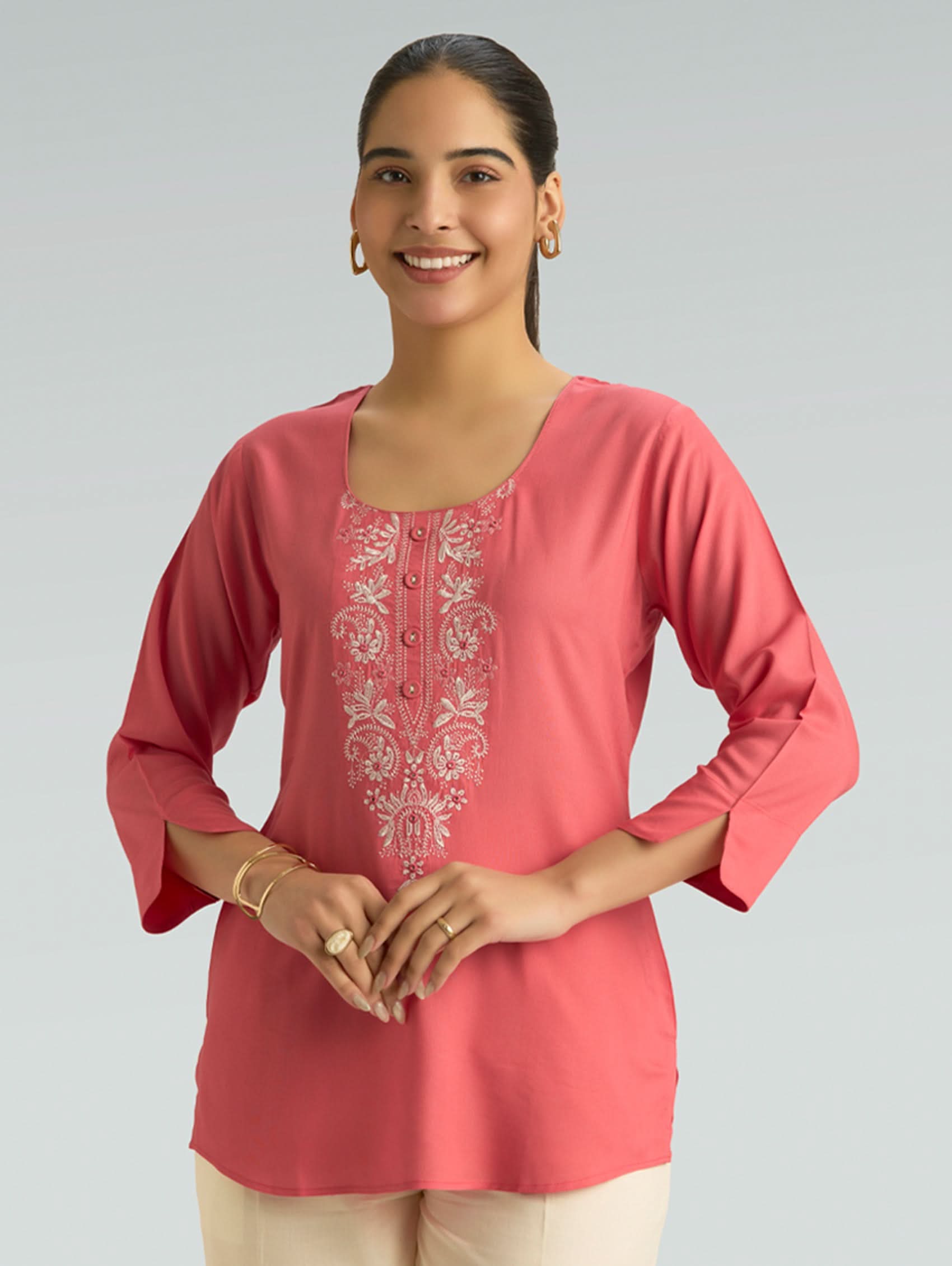 Woman wearing a pink embroidered top on a gray background