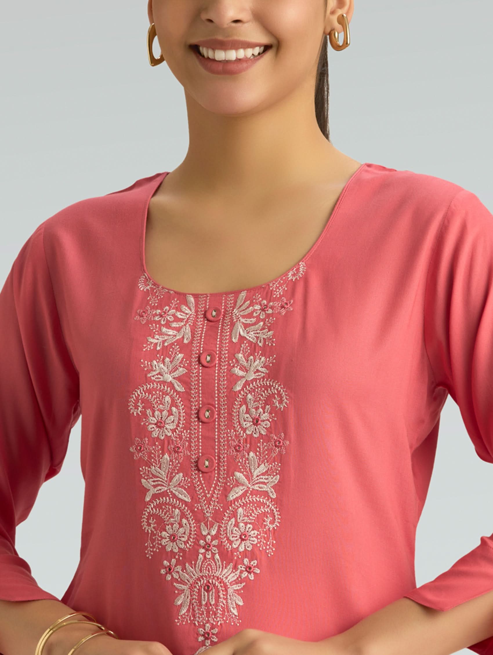 Woman wearing a pink top with white embroidery on a gray background