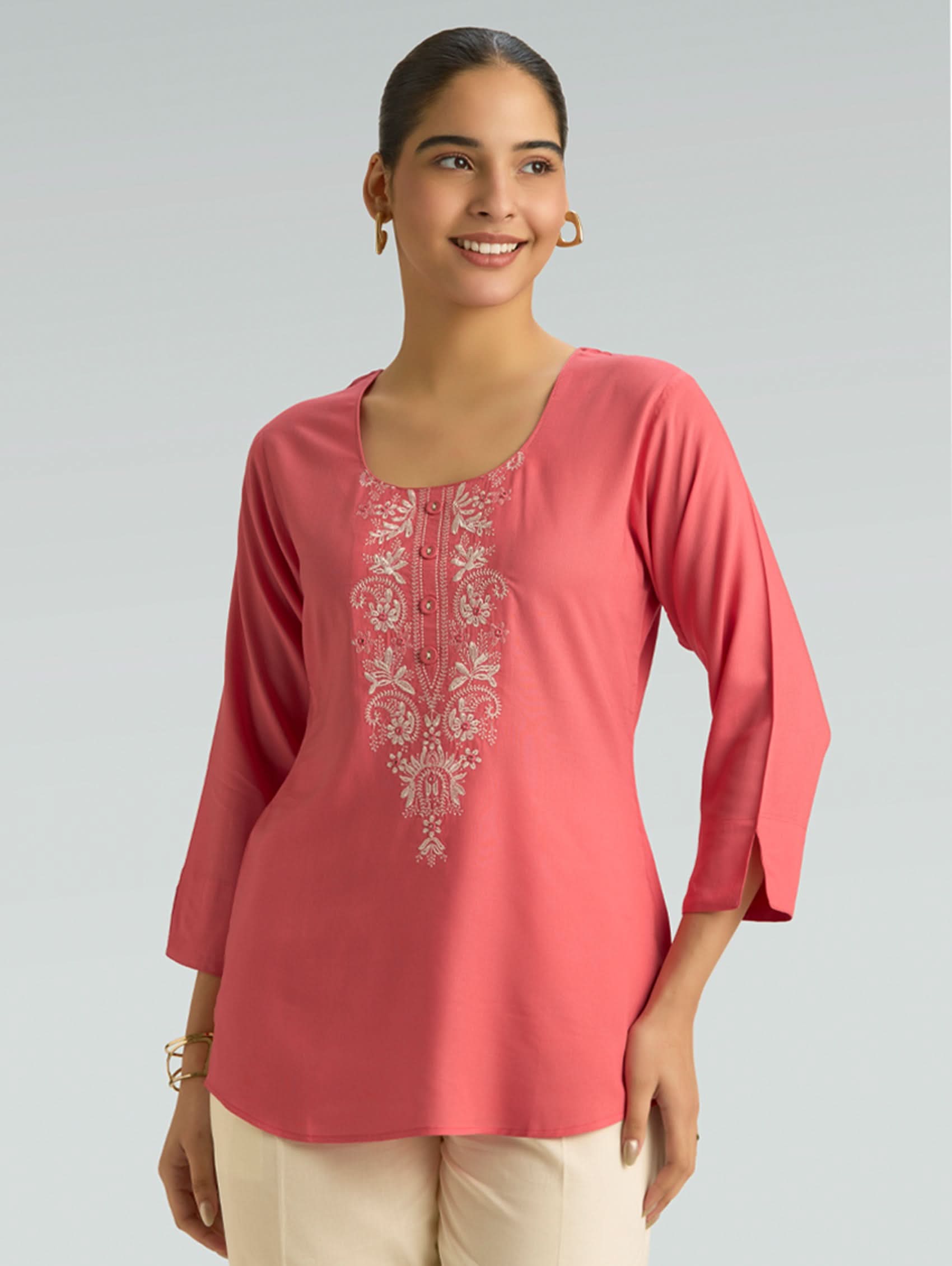 Woman wearing a pink embroidered top against a gray background