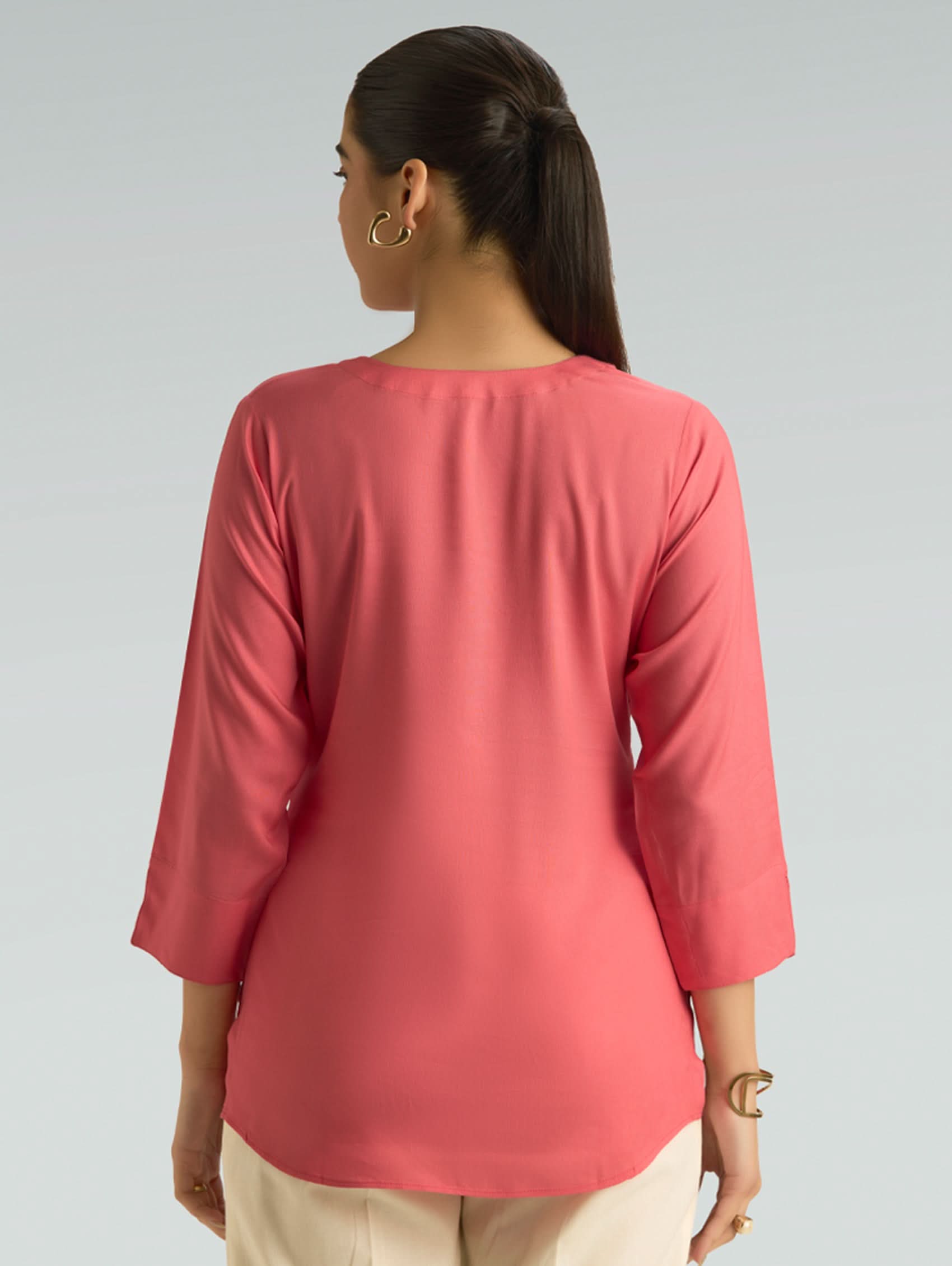 Person wearing a pink top with three-quarter sleeves on a gray background