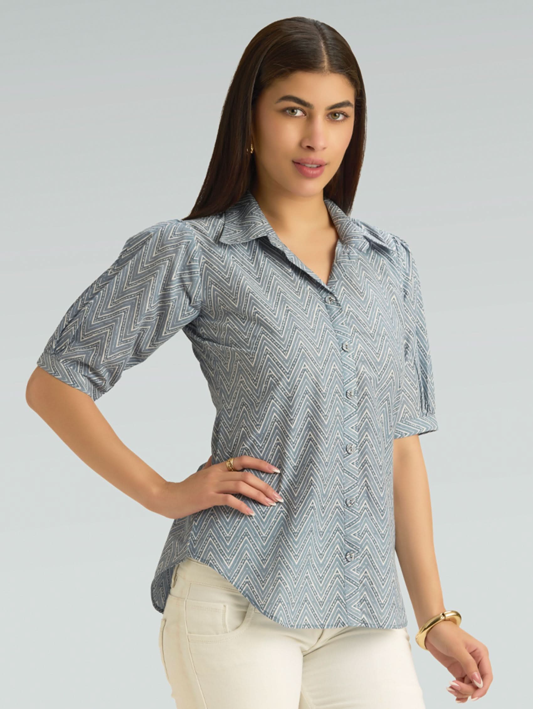 Woman wearing a patterned shirt and white pants on a gray background