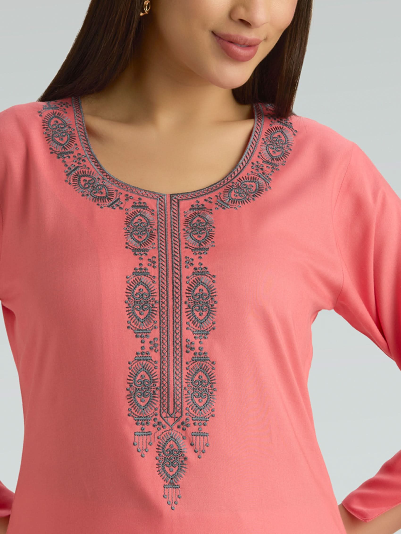 Woman wearing a flamingo pink kurta with a round neckline and intricate computer embroidery on a grey background