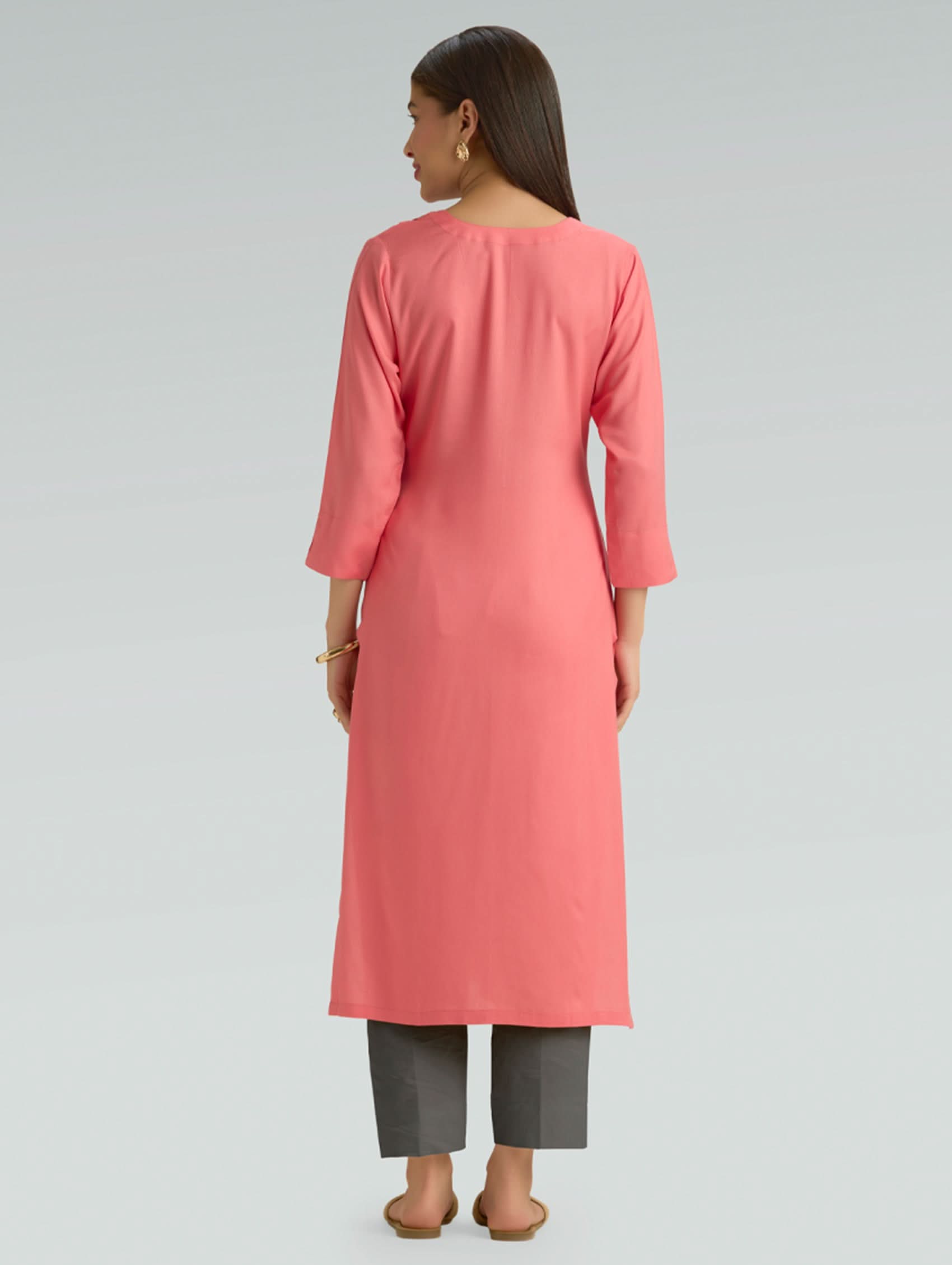 Woman wearing a pink kurta with gray pants on a light gray background