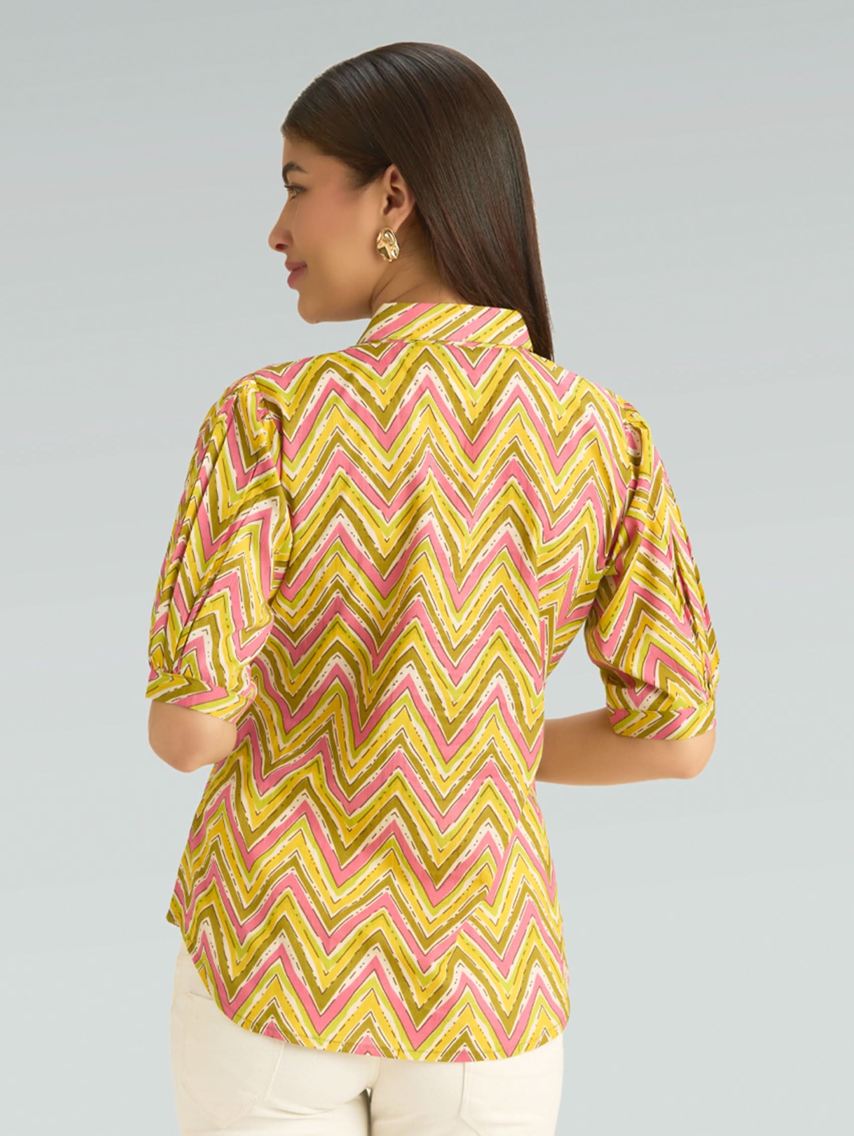 Woman wearing a yellow and pink zigzag patterned blouse against a gray background