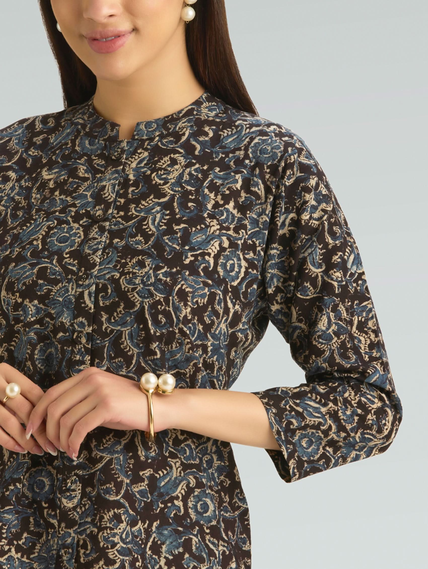 Woman wearing a patterned dress with pearl accessories on a gray background