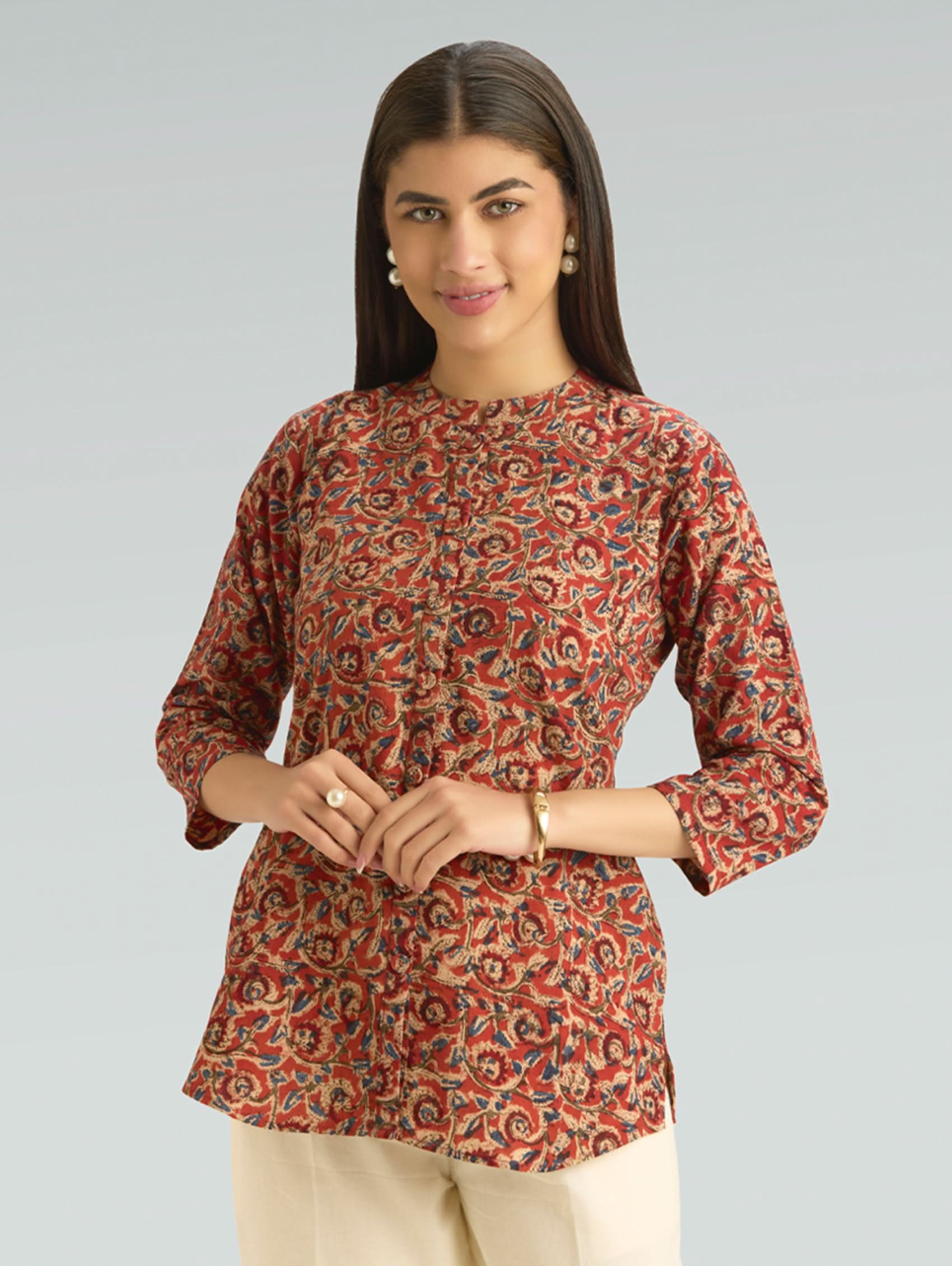 Woman wearing a patterned red and orange top against a gray background