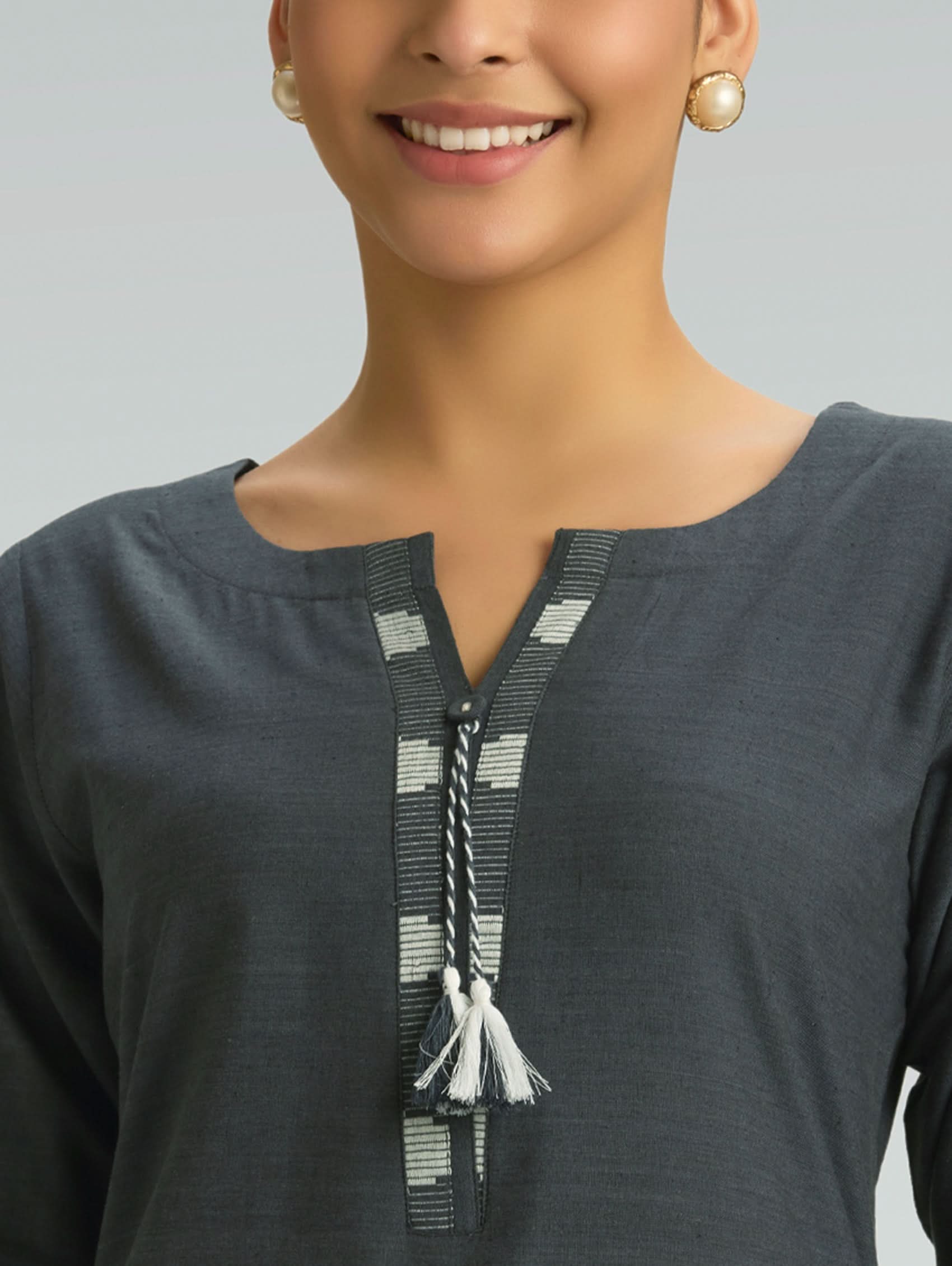 Woman wearing a dark gray top with decorative elements on a plain background