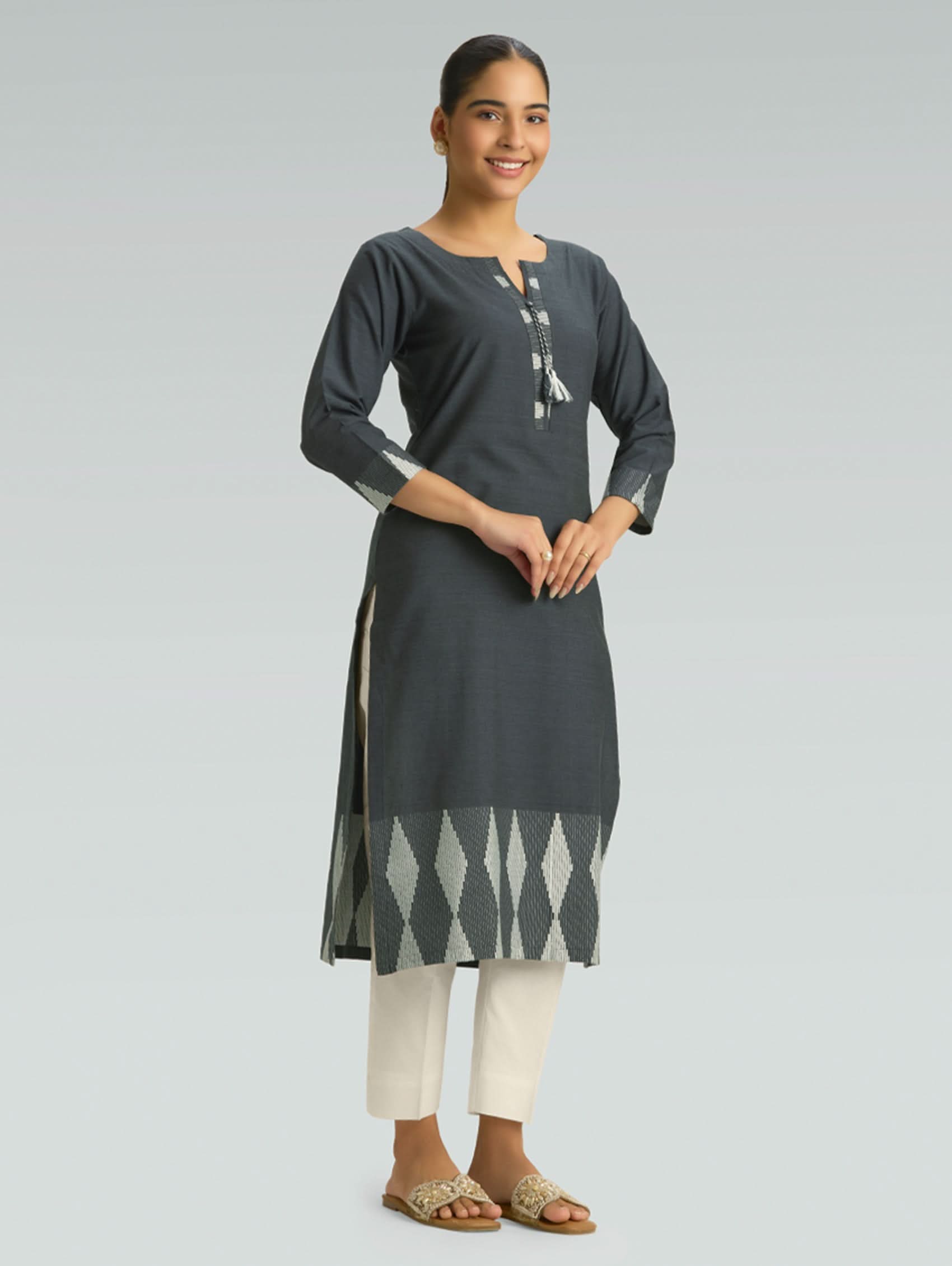 Woman wearing a dark gray kurta with white pants on a light gray background