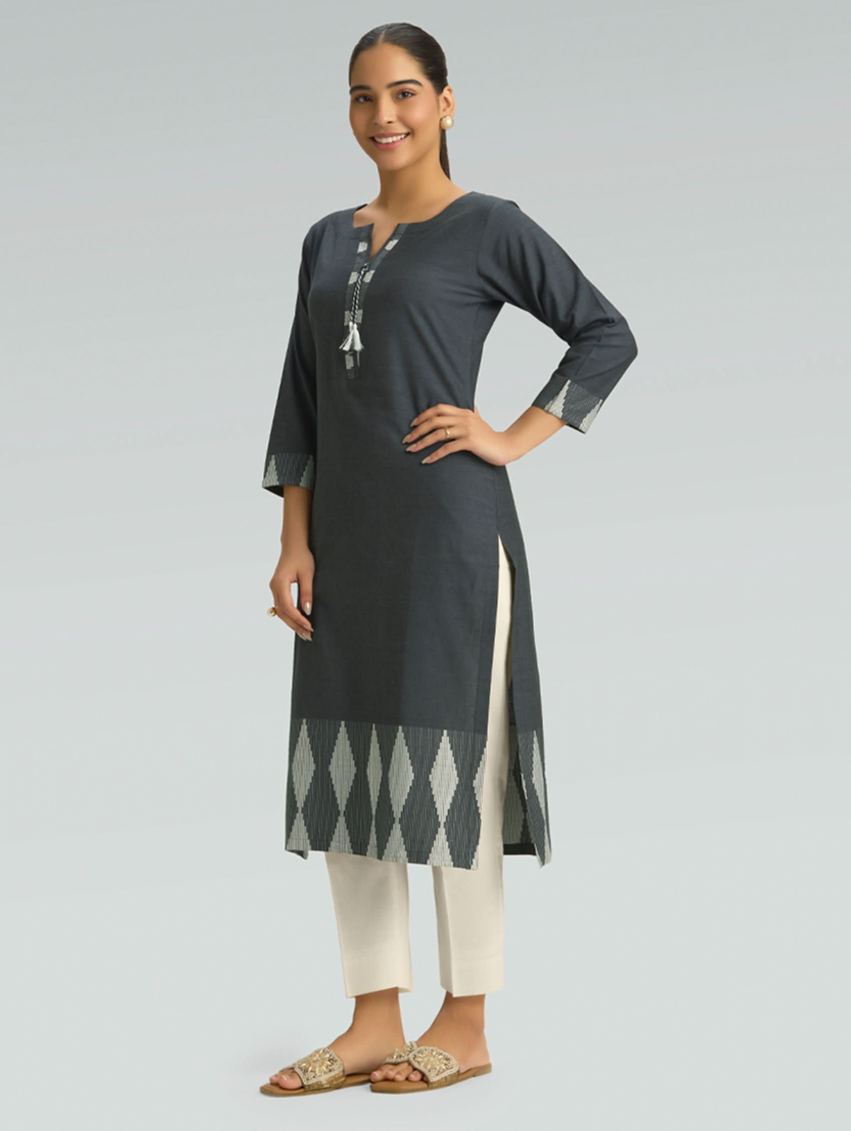 Woman wearing a dark gray kurta with white pants on a light gray background