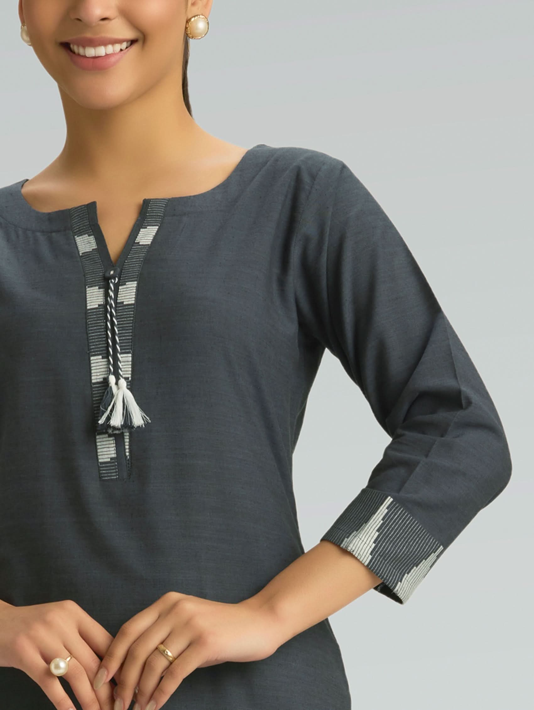 Woman wearing a dark gray top with intricate detailing on a light gray background