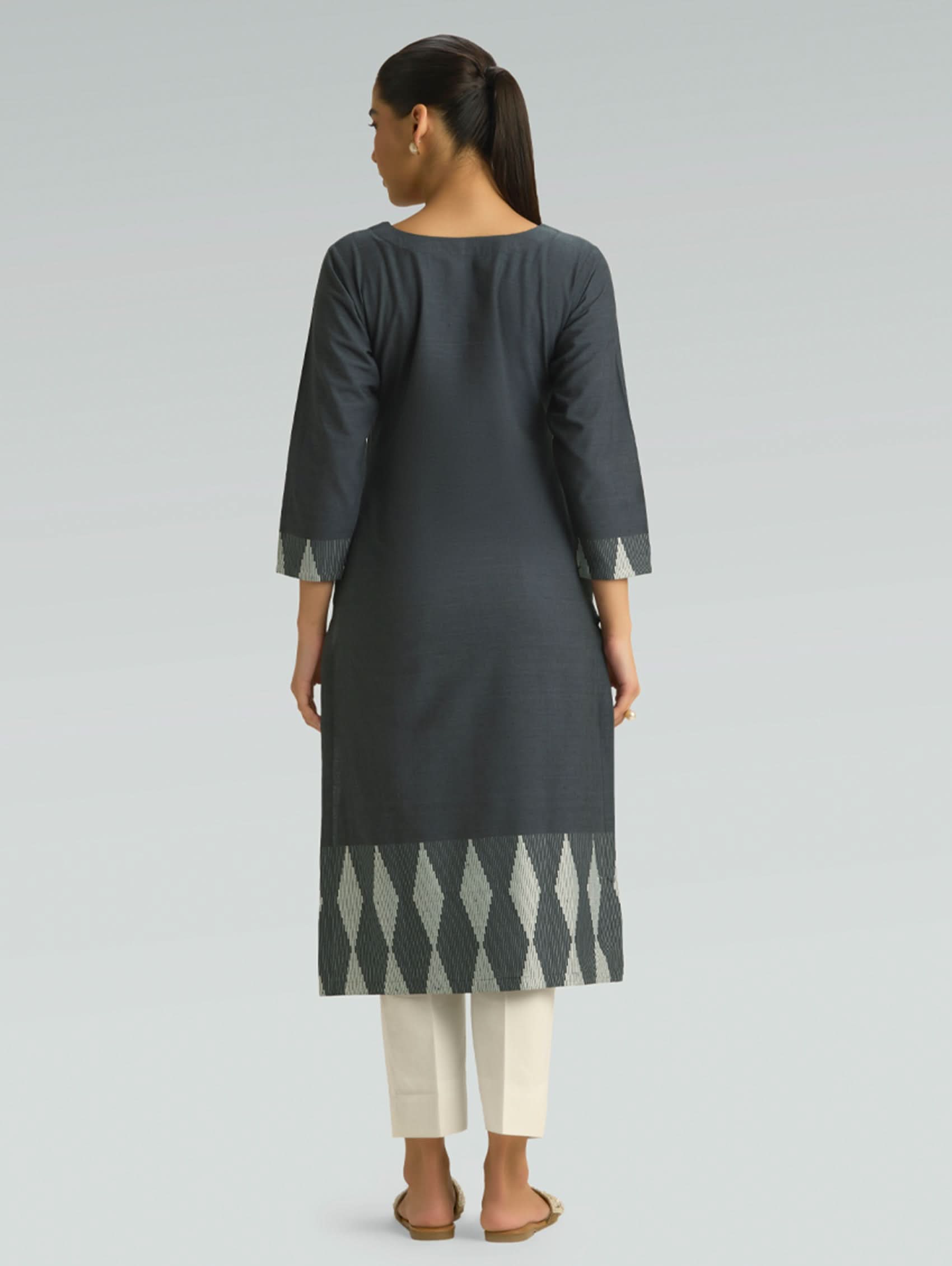 Woman wearing a dark gray kurta with white pants on a light gray background