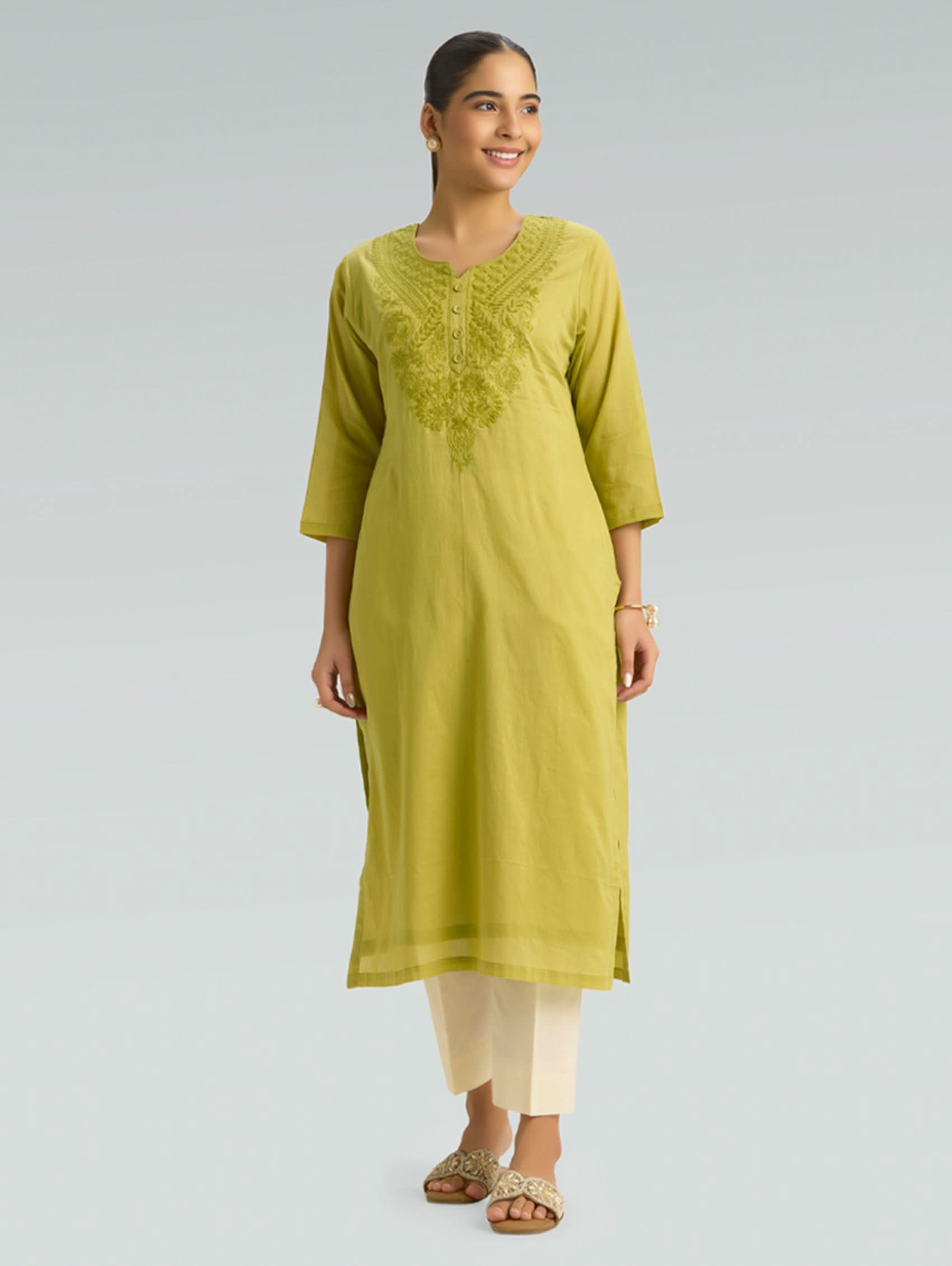 Woman wearing a green kurta with white pants on a gray background